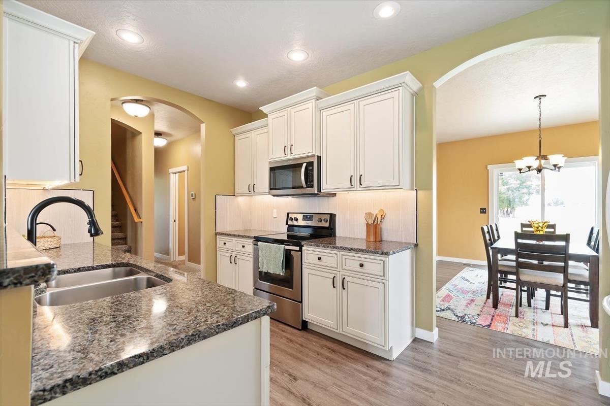 Kitchen with stainless steel appliances, arched walkways, light wood finished floors, white cabinets, and dark stone counters