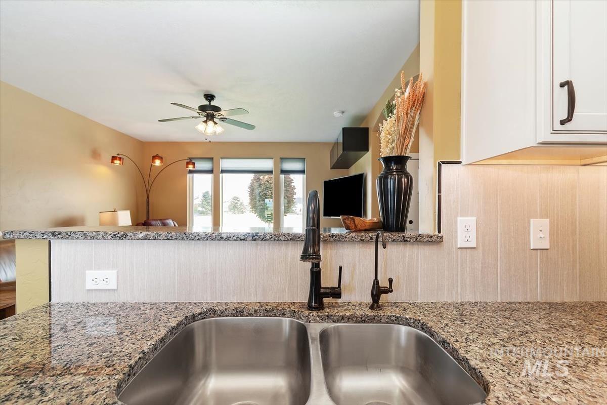 Kitchen featuring light stone counters, a ceiling fan, and white cabinetry