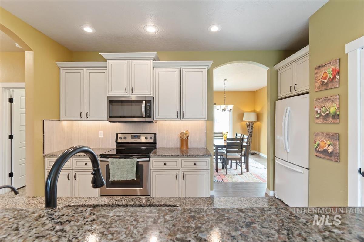 Kitchen featuring appliances with stainless steel finishes, arched walkways, recessed lighting, stone countertops, and white cabinets