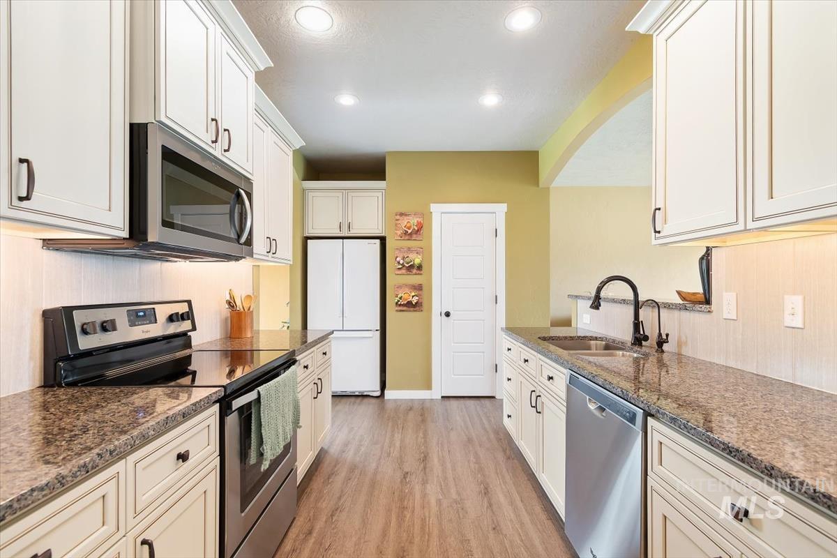 Kitchen with appliances with stainless steel finishes, light wood-type flooring, arched walkways, white cabinets, and recessed lighting