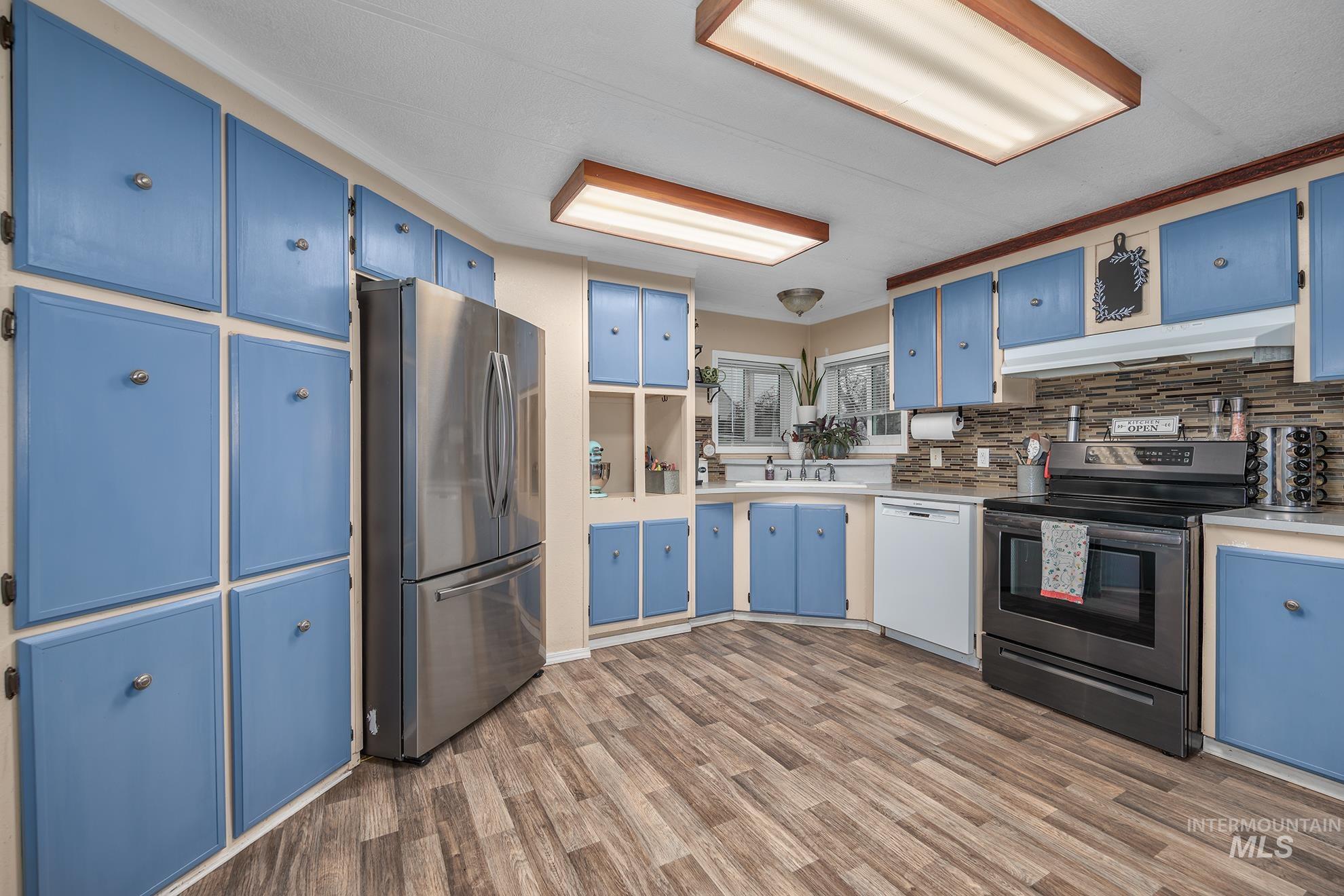 Kitchen with blue cabinetry, stainless steel appliances, light countertops, and under cabinet range hood
