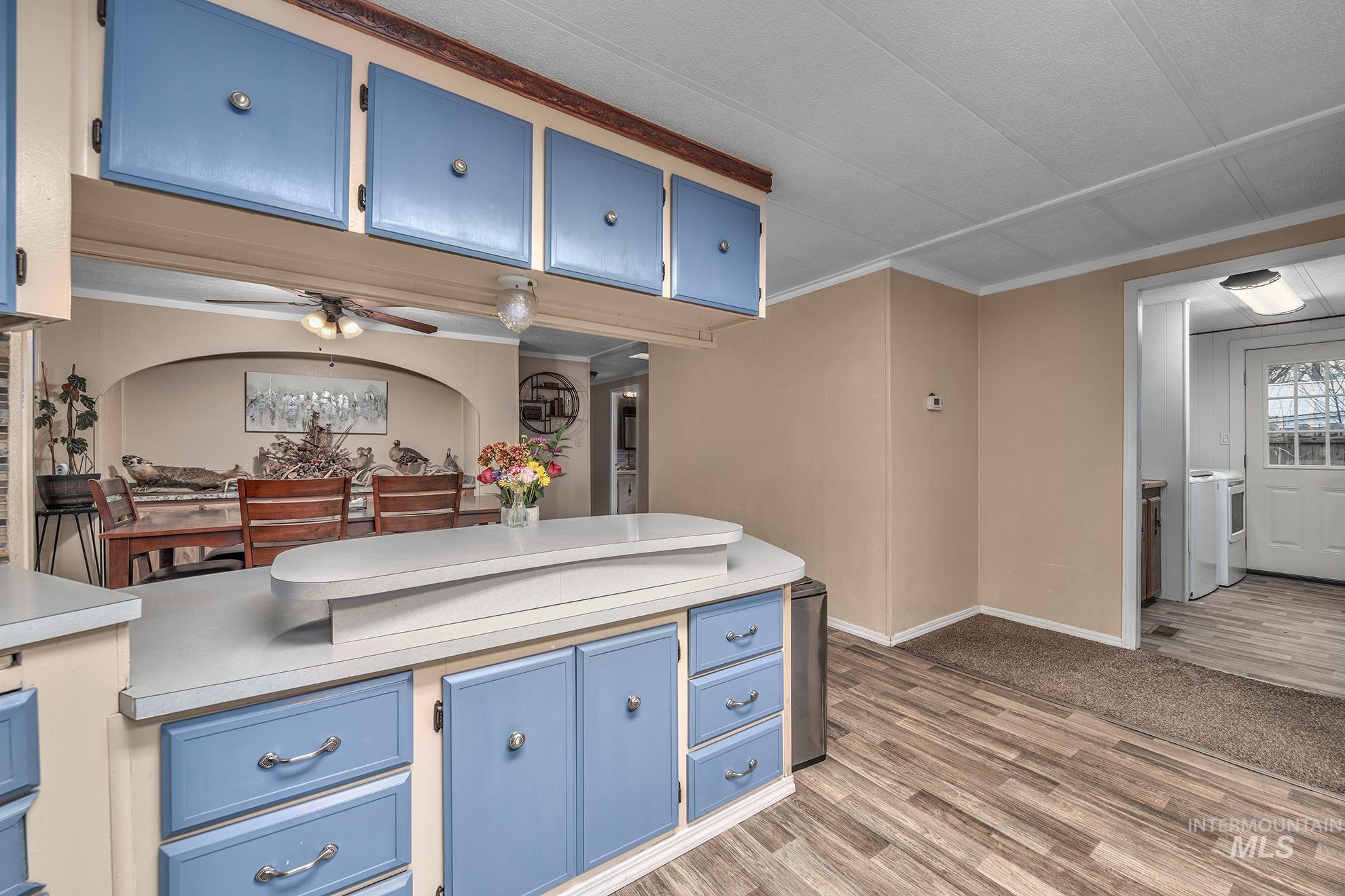 Kitchen with blue cabinetry, light countertops, light wood-style flooring, a ceiling fan, and ornamental molding