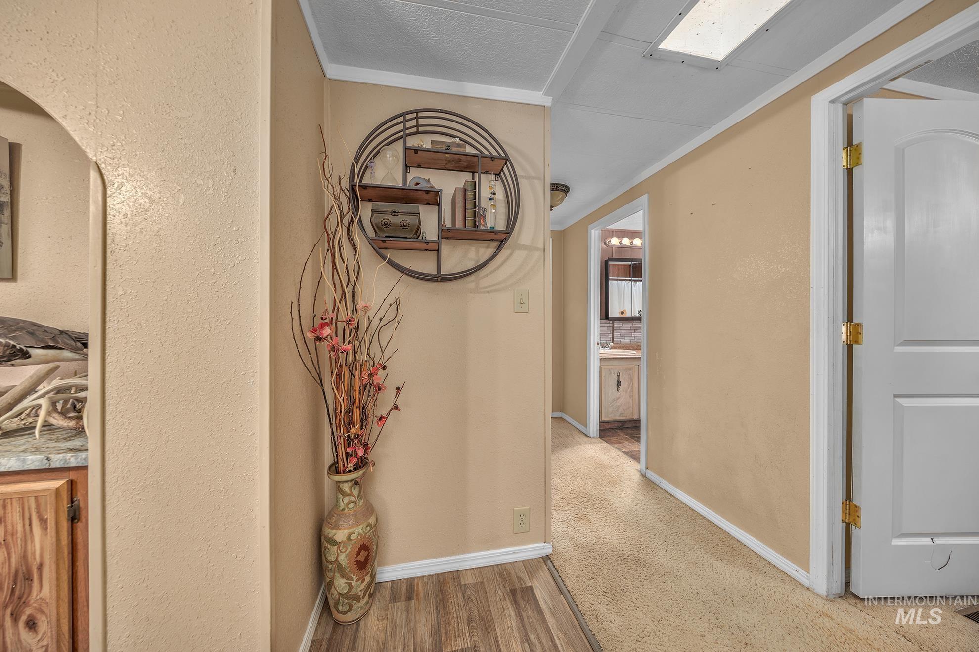 Hallway with wood finished floors, a textured wall, and crown molding