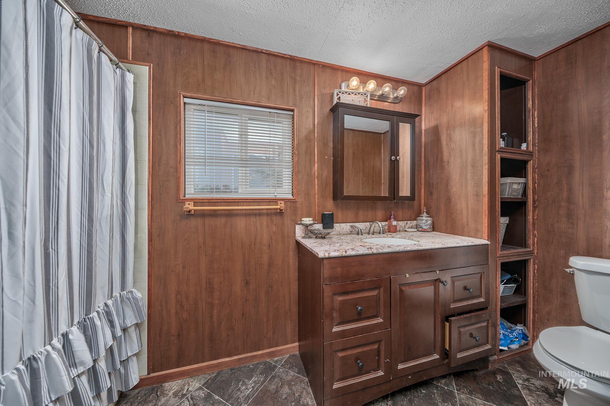 Bathroom featuring a shower with curtain, wooden walls, a textured ceiling, and vanity