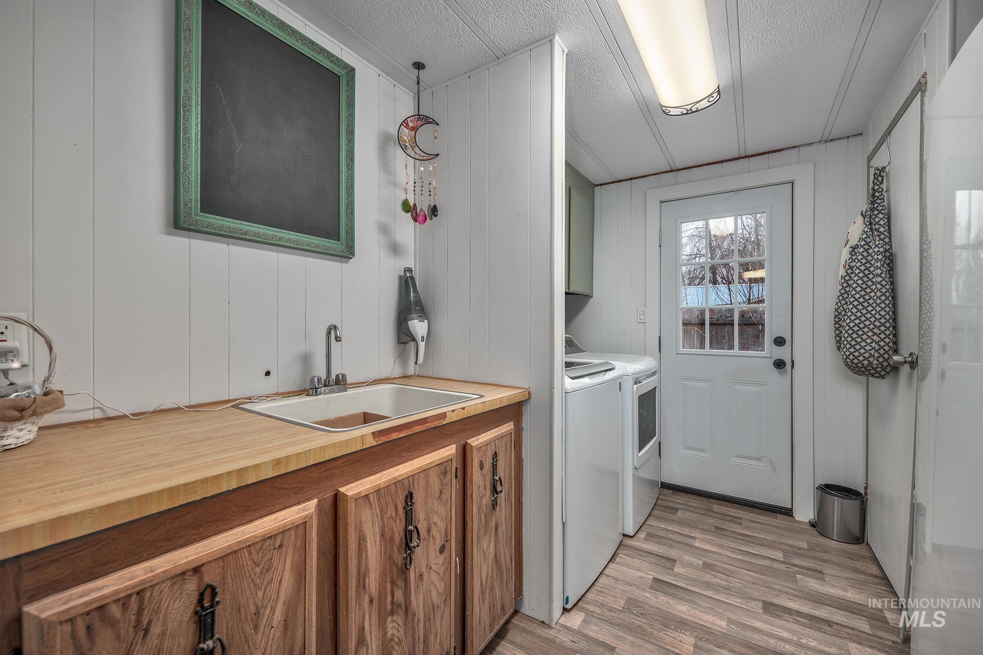Washroom featuring cabinet space, light wood-style flooring, washing machine and dryer, wooden walls, and a textured ceiling