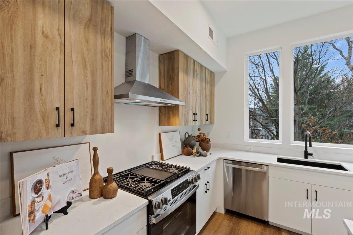 Kitchen featuring stainless steel appliances, wall chimney range hood, light stone countertops, and light wood-type flooring