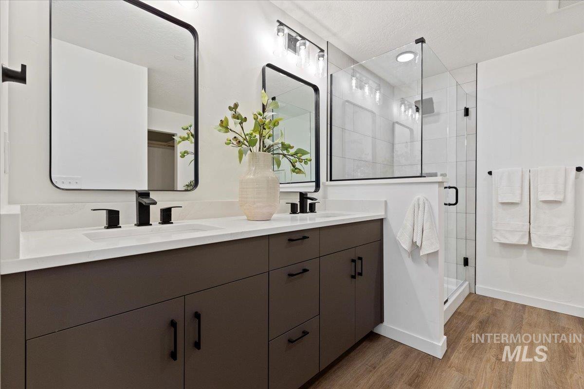 Bathroom featuring a shower stall, double vanity, light wood finished floors, and a textured ceiling
