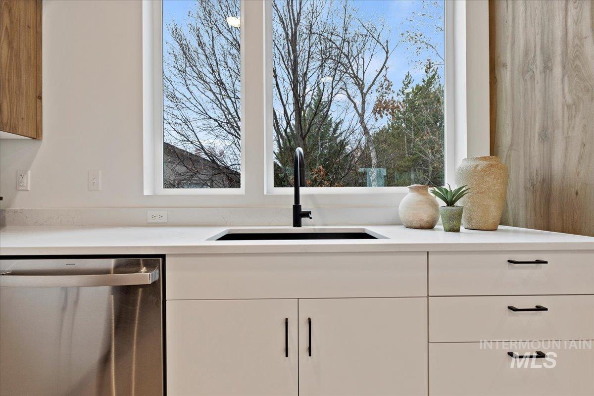 Kitchen view of stainless steel dishwasher, white cabinets, and light stone countertops