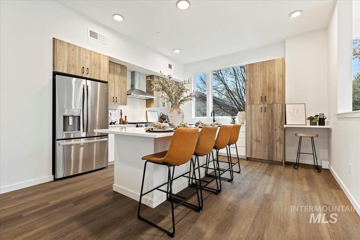 Kitchen featuring stainless steel refrigerator with ice dispenser, a breakfast bar area, a center island, light brown cabinets, and modern cabinets