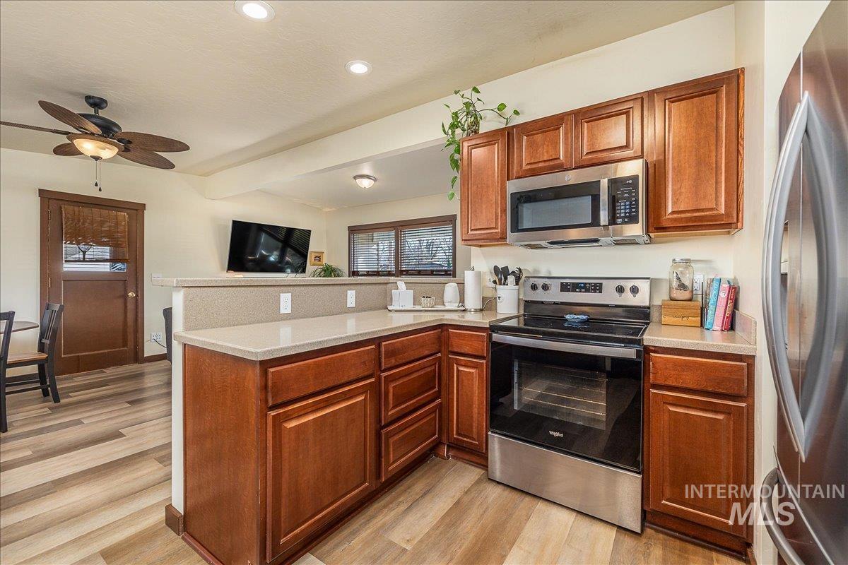 Kitchen with a peninsula, stainless steel appliances, ceiling fan, wood finish cabinetry, and light wood-type flooring