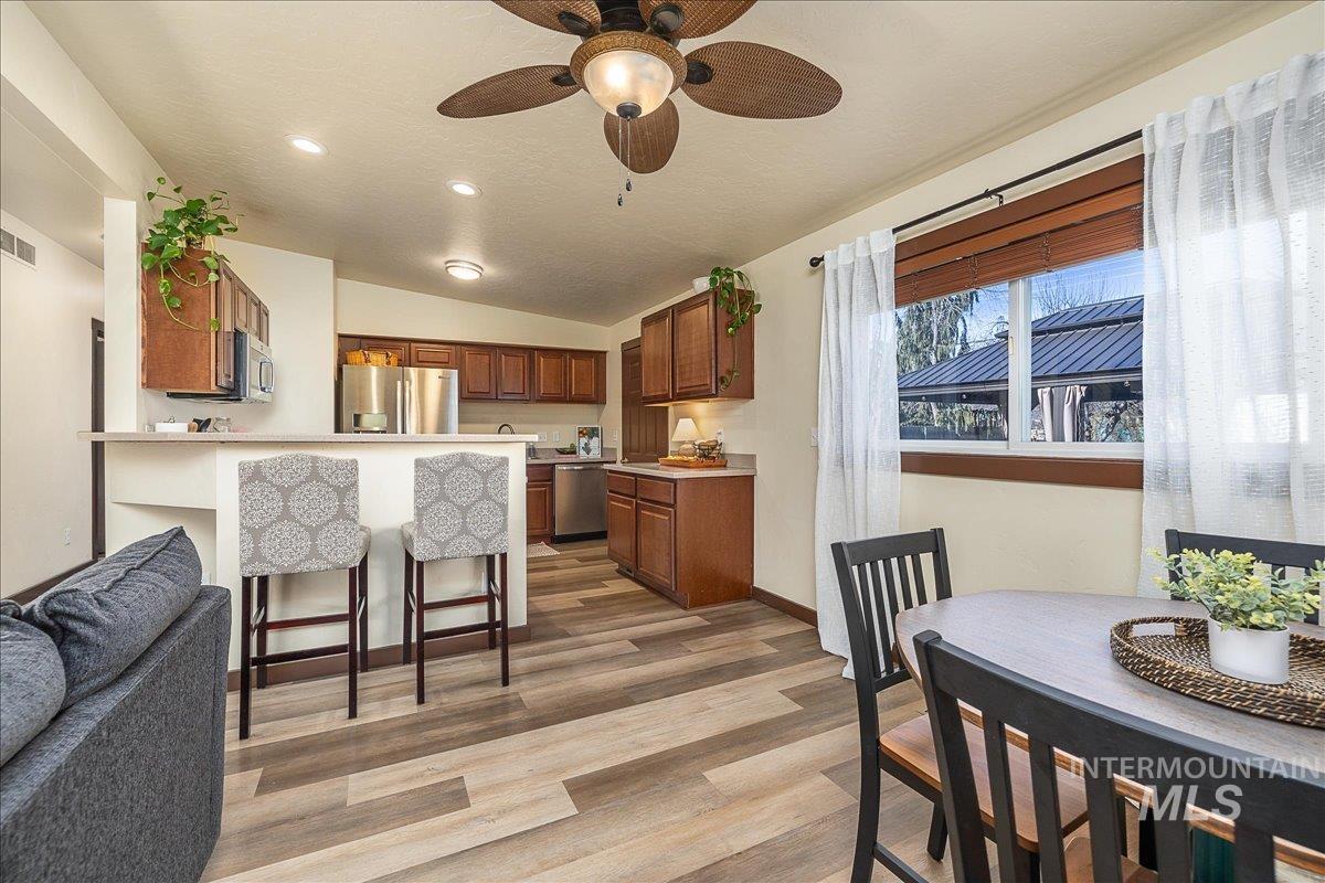 Kitchen featuring wood finish cabinets, ceiling fan, a breakfast bar area, lofted ceiling, and light wood-style flooring