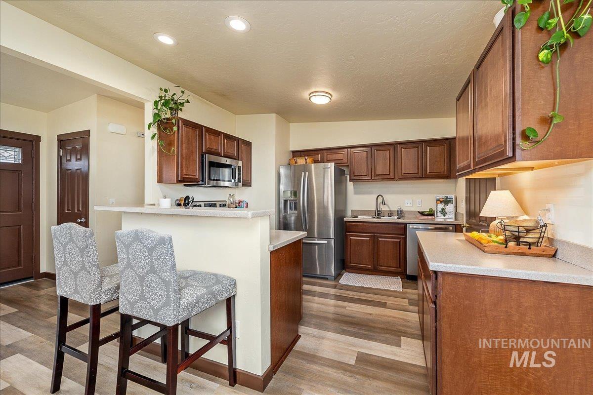 Kitchen with stainless steel appliances, light countertops, a breakfast bar, light wood-style floors, and a textured ceiling