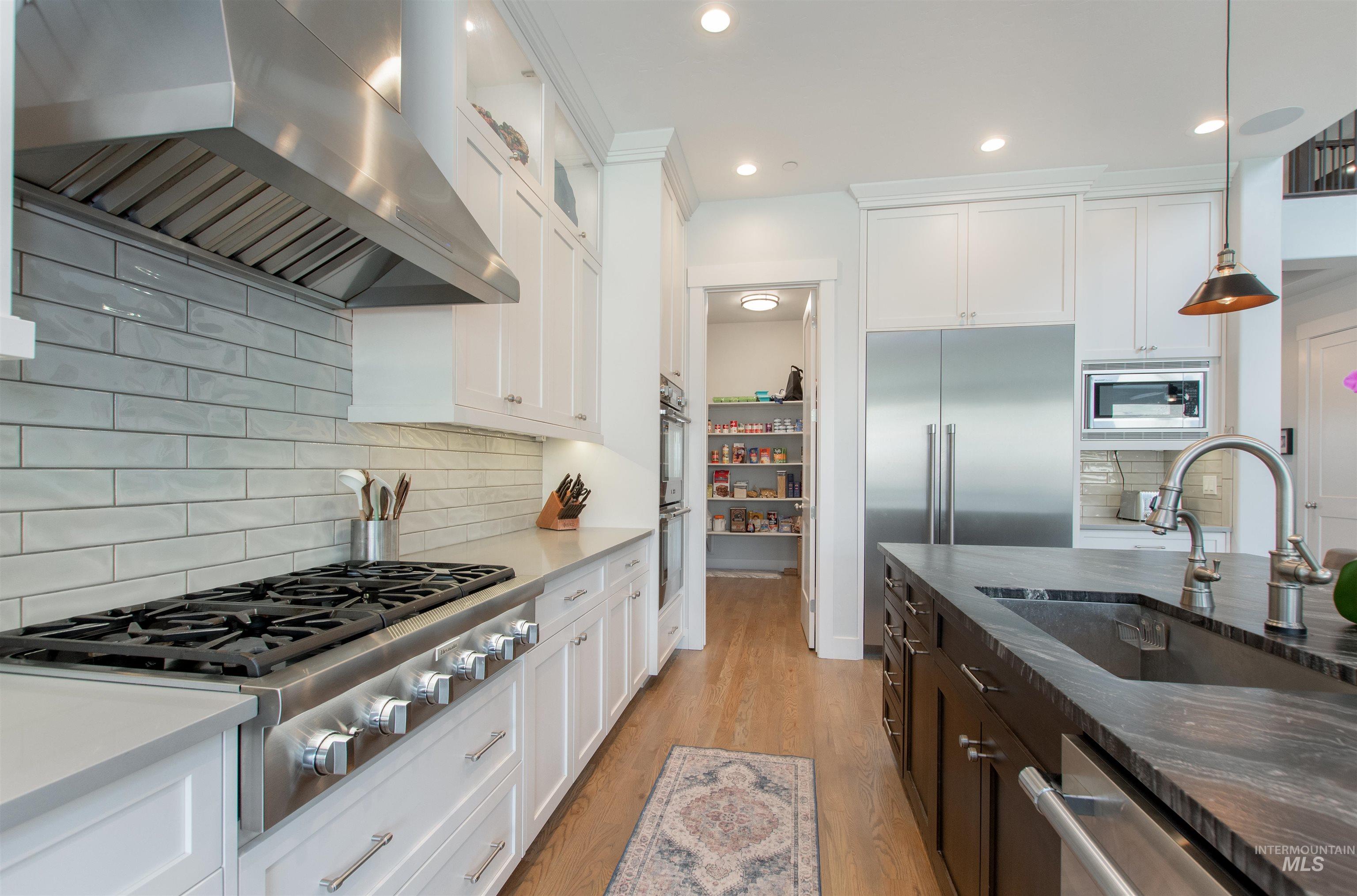 Kitchen with range hood, dark stone counters, decorative backsplash, pendant lighting, and built in appliances