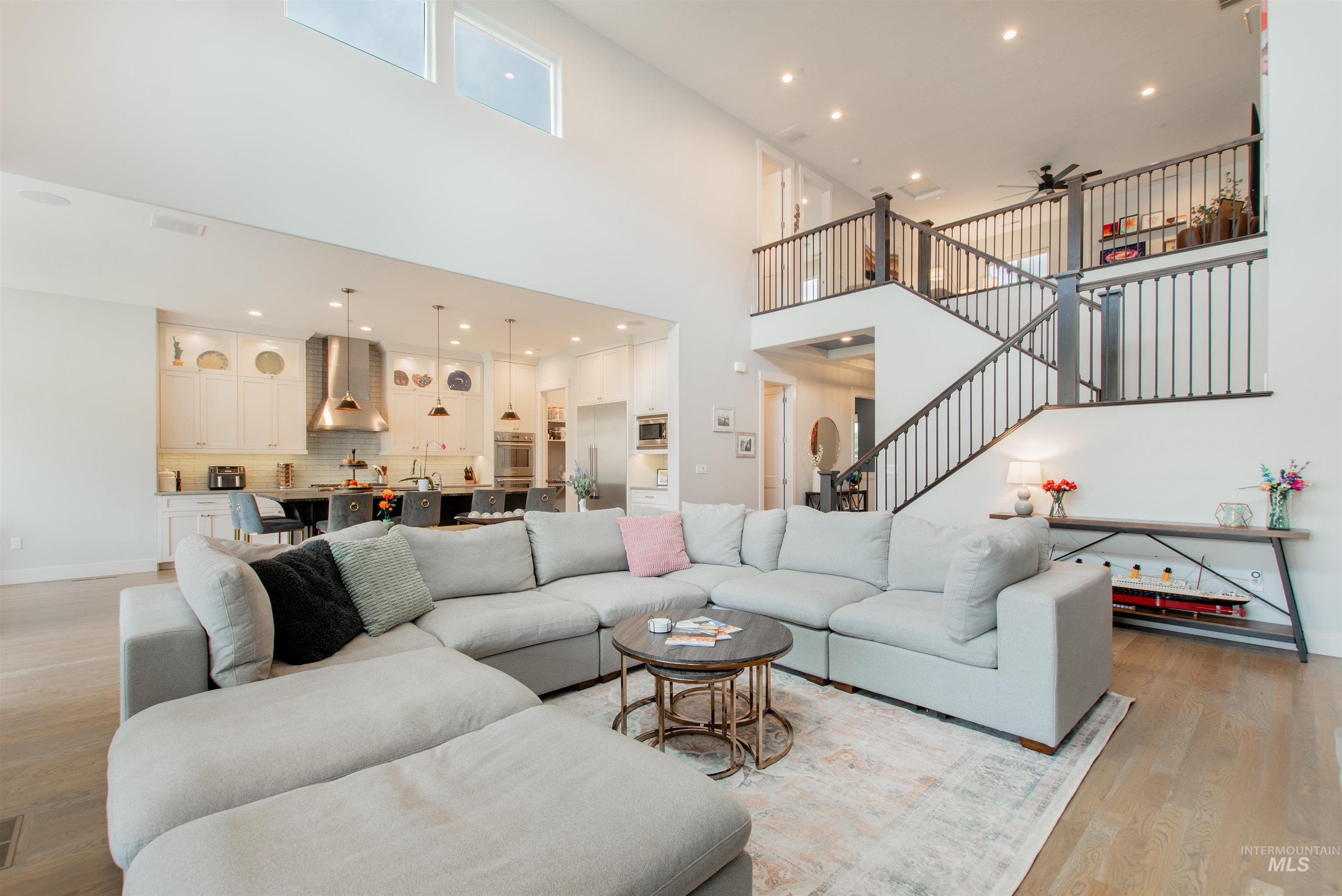 Living room featuring light wood finished floors, stairway, ceiling fan, recessed lighting, and a high ceiling