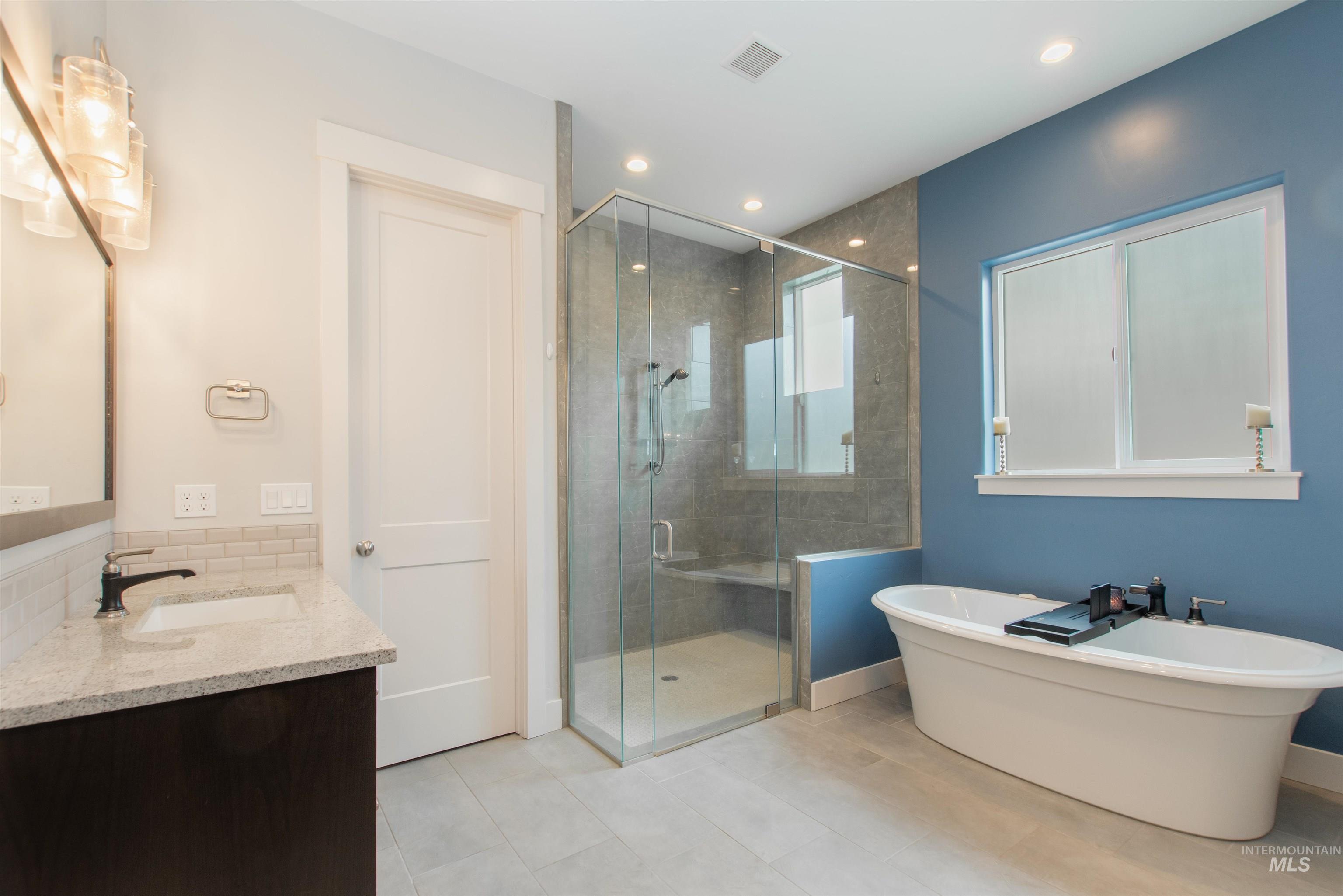 Full bath with vanity, a freestanding bath, a stall shower, light tile patterned flooring, and recessed lighting
