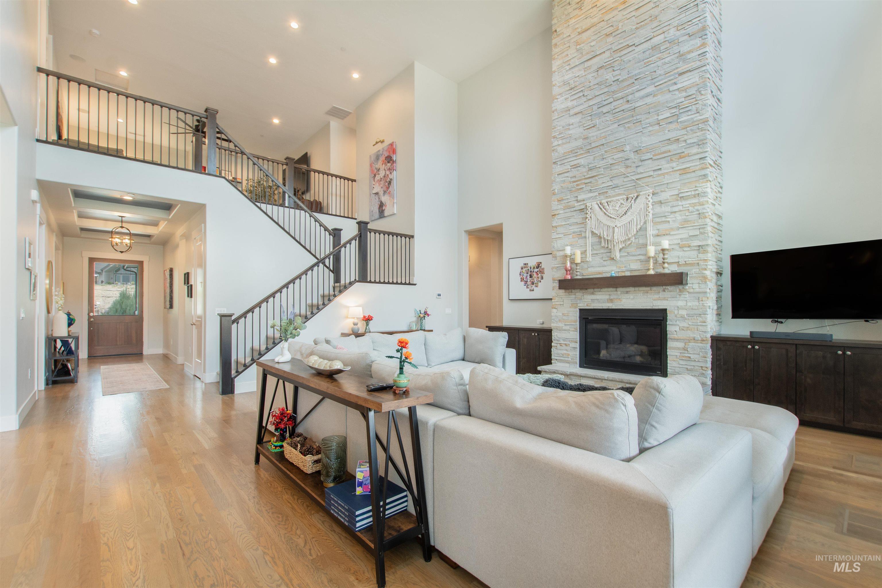 Living room with light wood-style flooring, stairs, a fireplace, a towering ceiling, and recessed lighting
