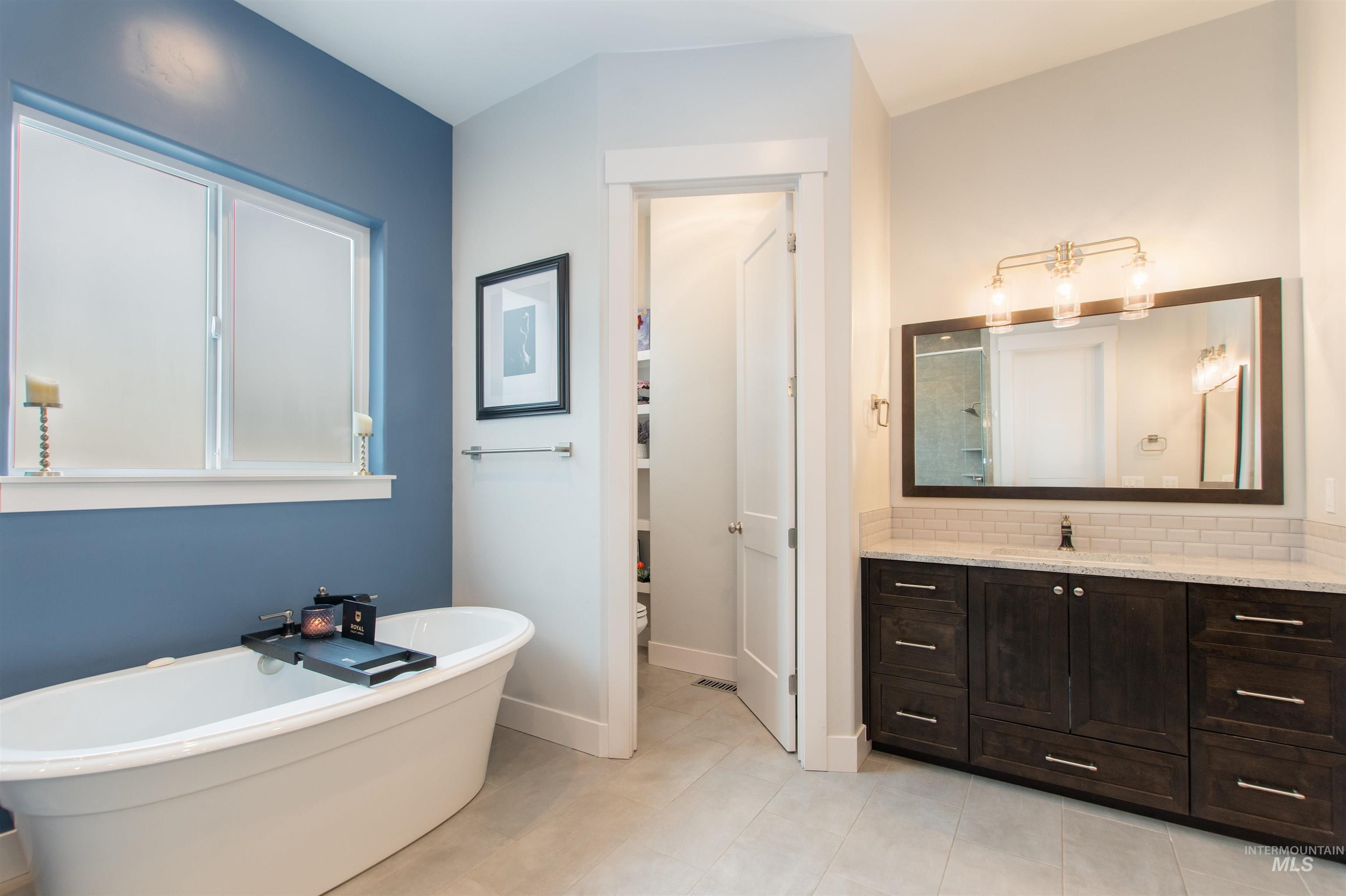 Full bath featuring a freestanding tub, vanity, a stall shower, light tile patterned floors, and tasteful backsplash