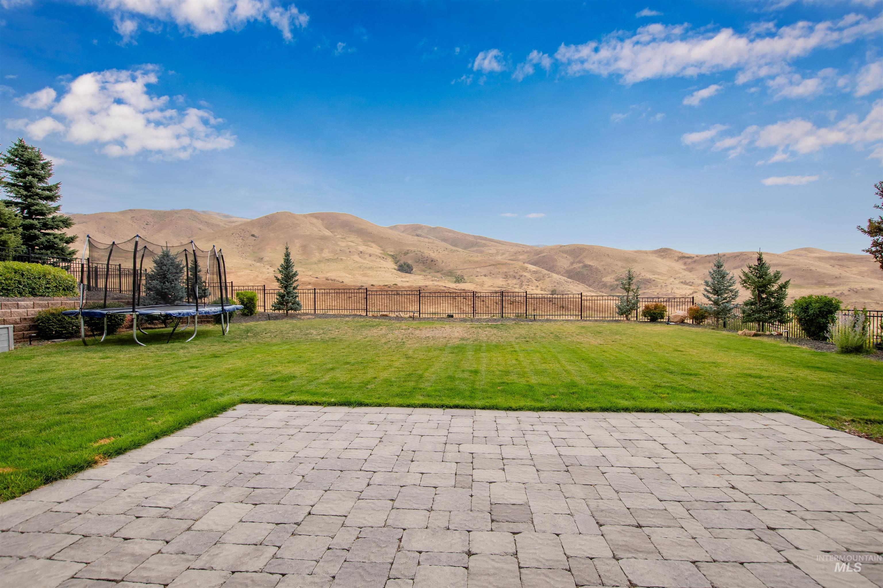 Fenced backyard with a mountain view, a patio, a trampoline, and a view of rural / pastoral area