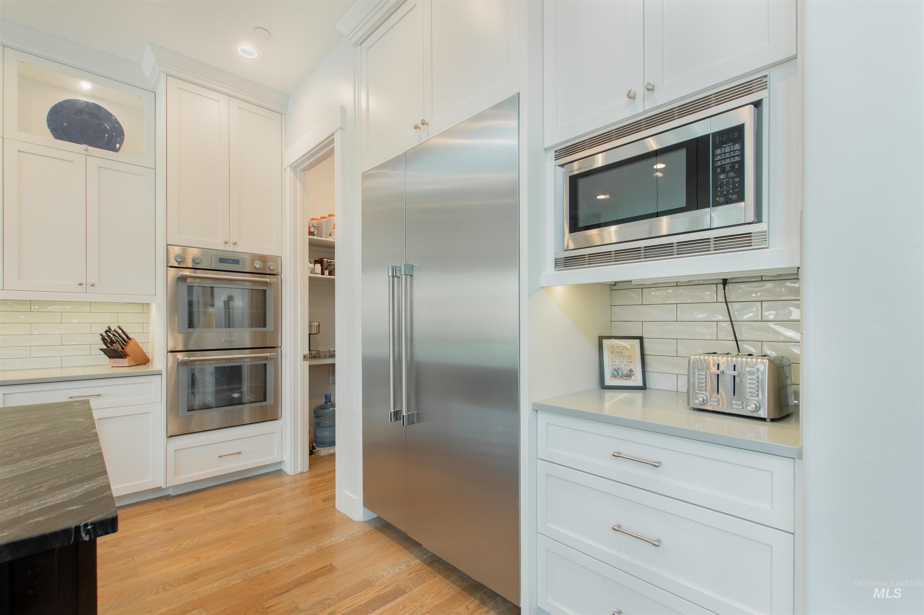 Kitchen featuring decorative backsplash, built in appliances, white cabinetry, dark stone counters, and recessed lighting