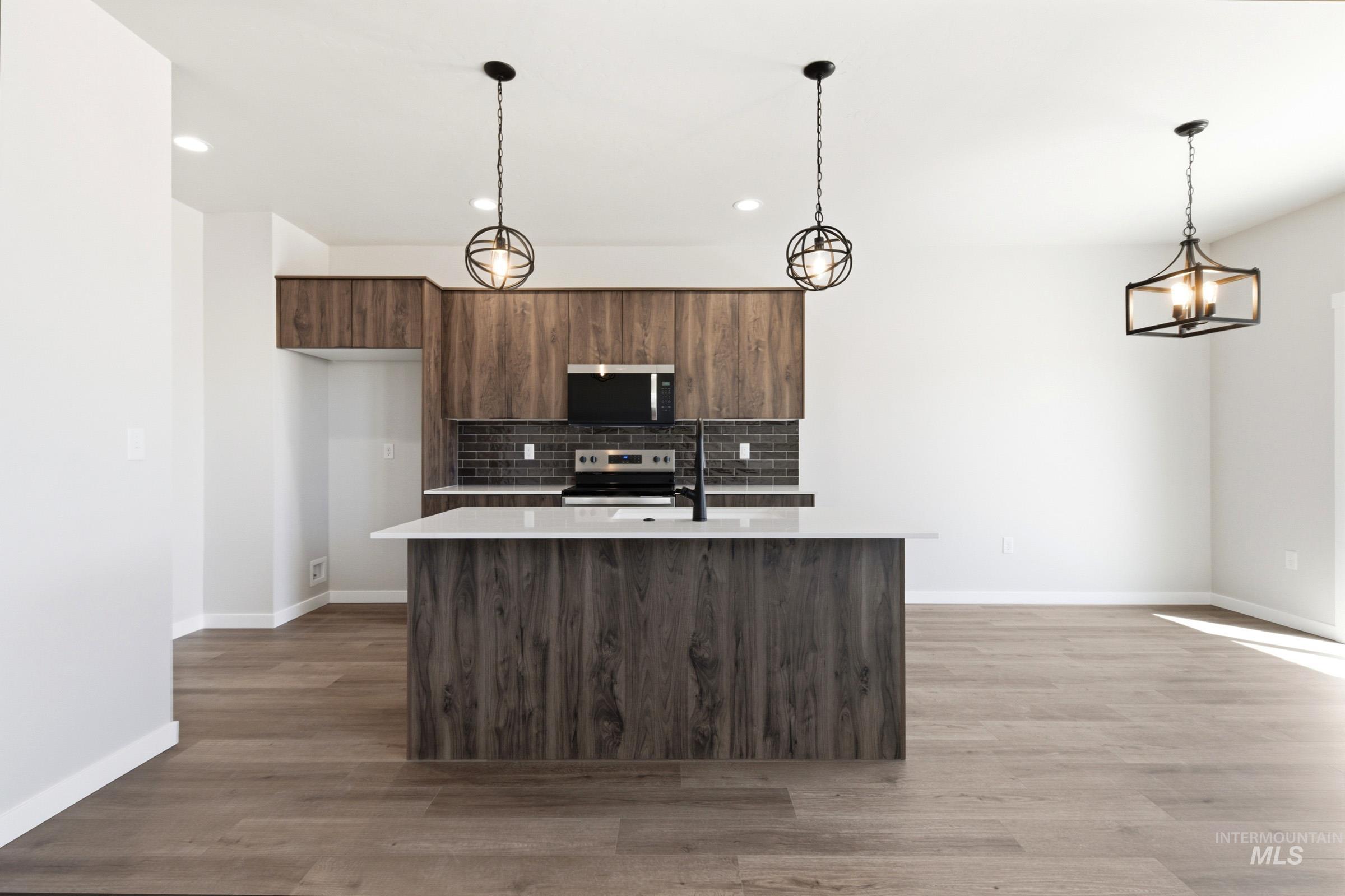 Modern kitchen featuring wood-finish cabinetry, a white countertop island with an integrated sink, and a black subway tile backsplash