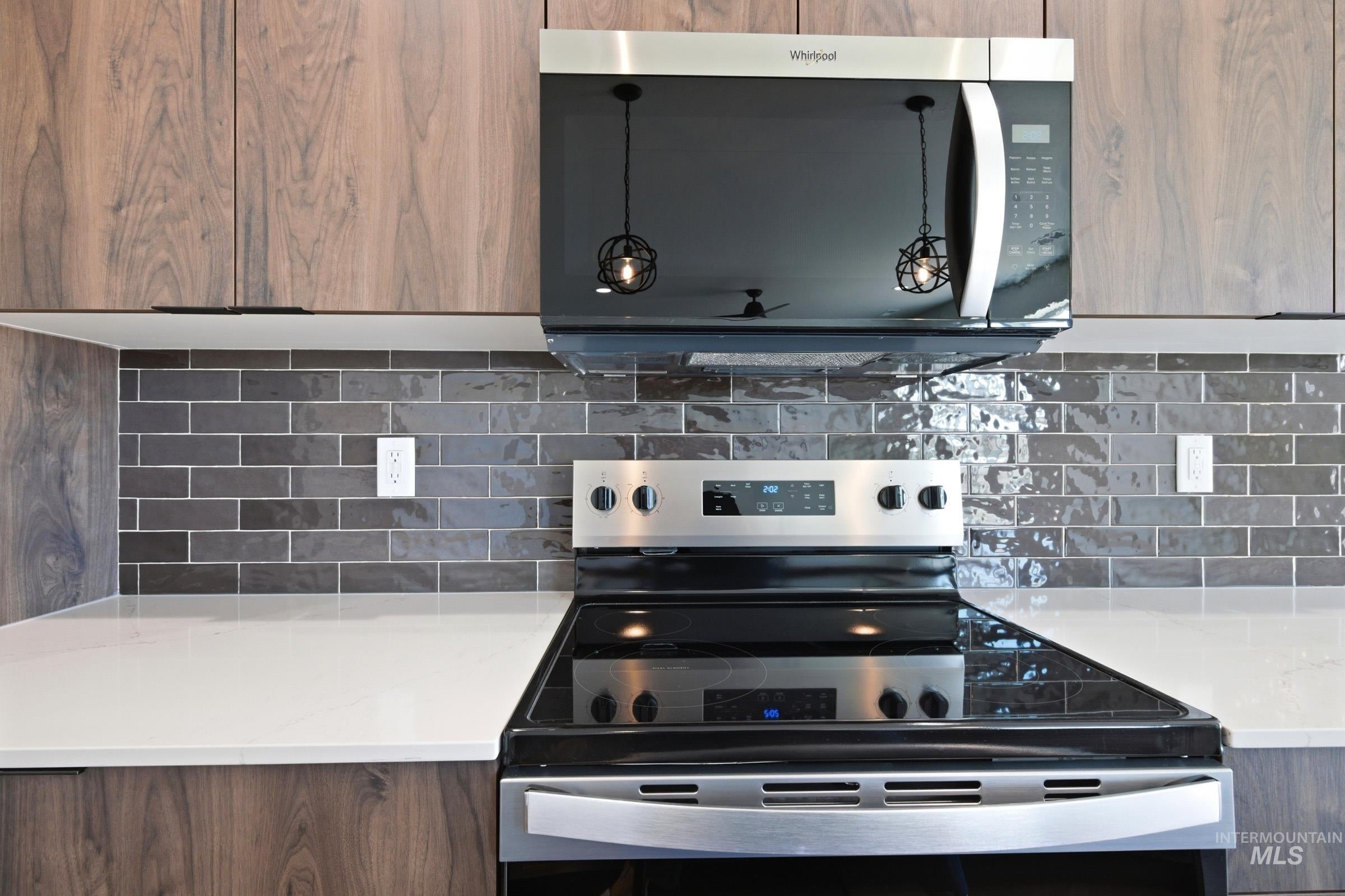 Kitchen featuring wood-finish cabinetry, a stainless steel range, a coordinating over-the-range microwave, white countertops, and a gray subway tile backsplash