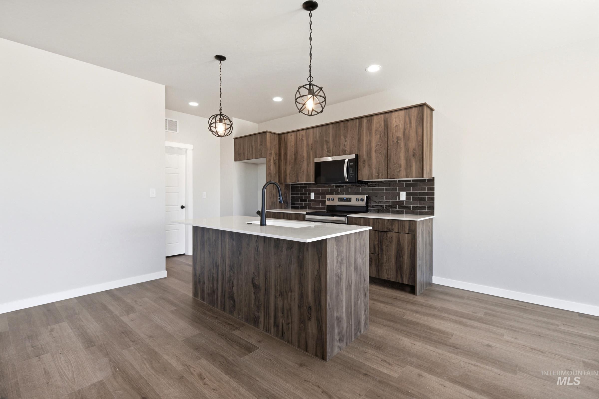 Kitchen featuring a central island with a light-toned countertop and black faucet, wood-finish cabinetry, dark subway tile backsplash, and stainless steel appliances
