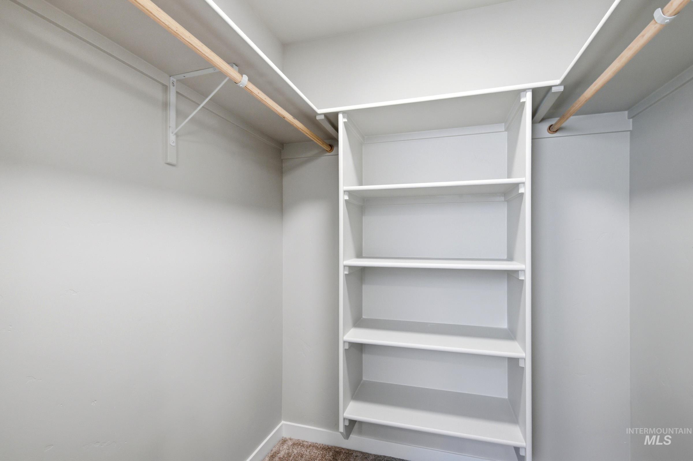 Built-in white shelving system featuring five adjustable shelves, complemented by natural wood hanging rods and light gray wall paint