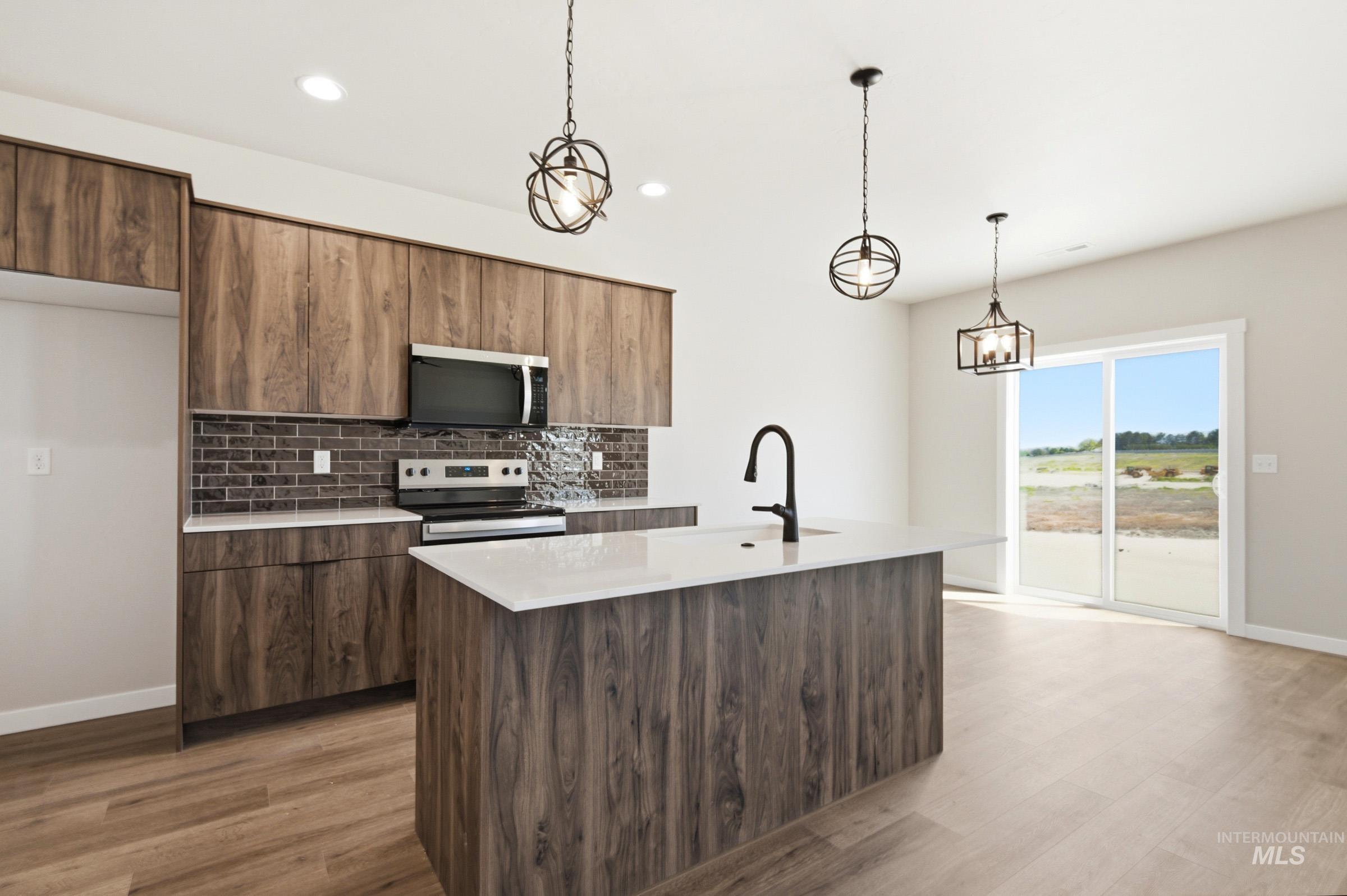 Kitchen featuring wood-finish cabinetry, quartz countertops, a brick-patterned backsplash, stainless steel appliances, and a central island with an integrated sink