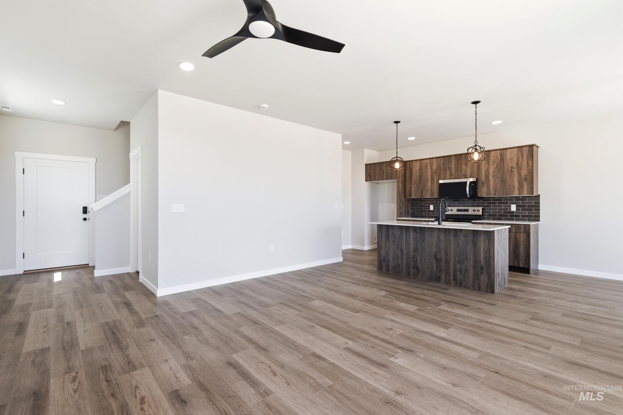 Open-concept living space featuring wood-finish flooring, a modern kitchen with a central island, dark wood-finish cabinetry, stainless steel appliances, and pendant lighting