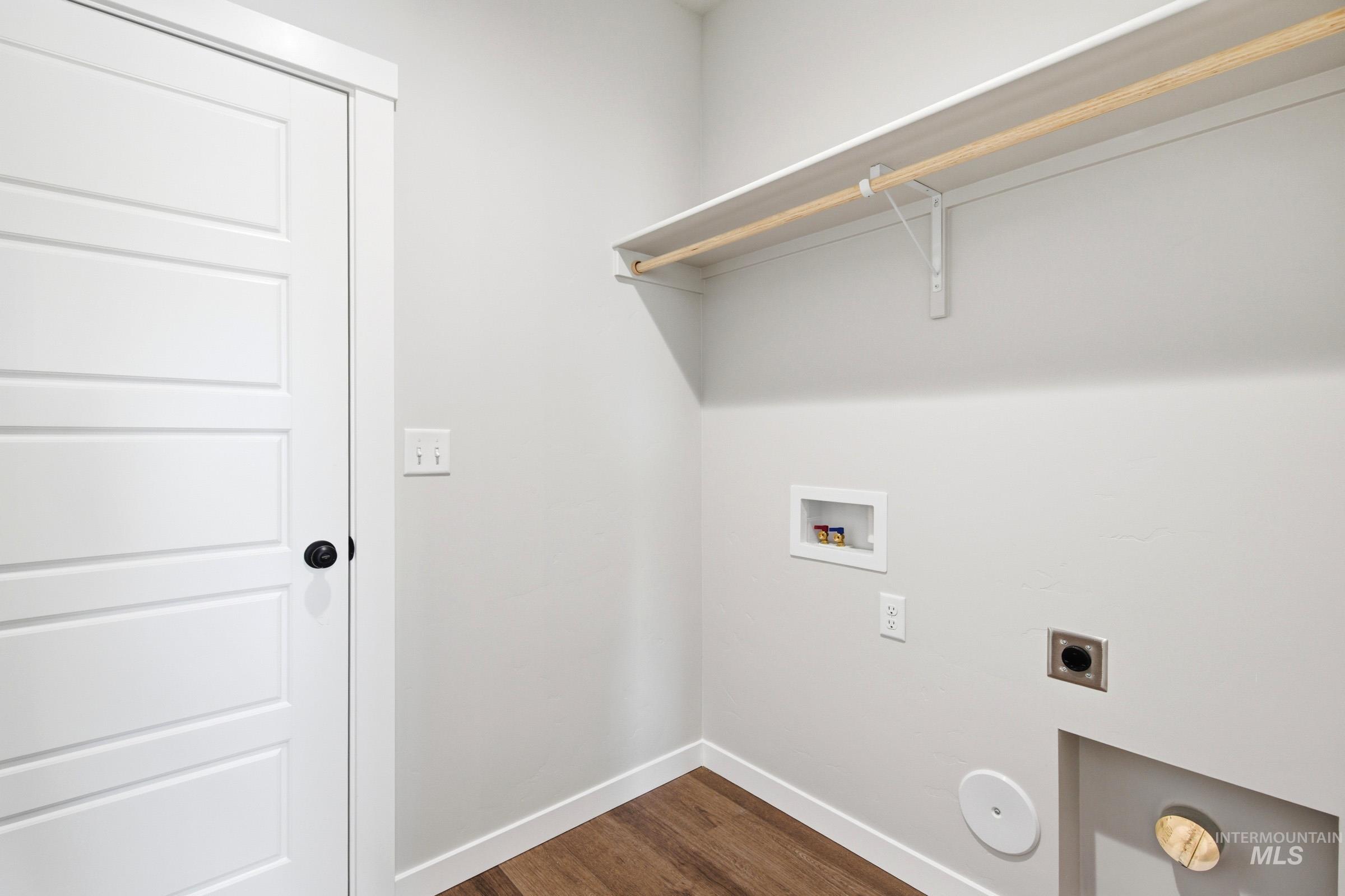 Utility area featuring wood-finish flooring, light gray walls, a white four-panel door with a black knob, and a built-in shelf and hanging rod