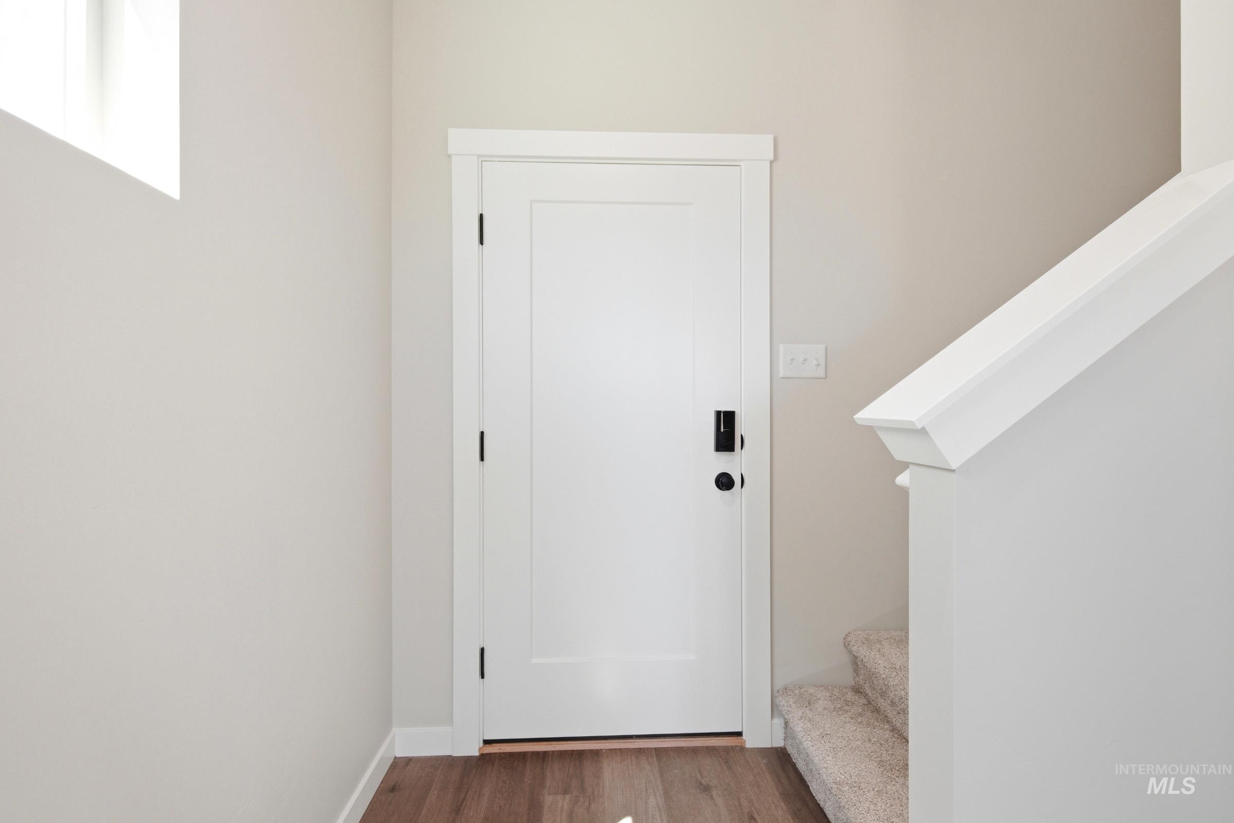 Entryway featuring a white paneled door with black hardware, wood-finish flooring, and a carpeted staircase with a white railing