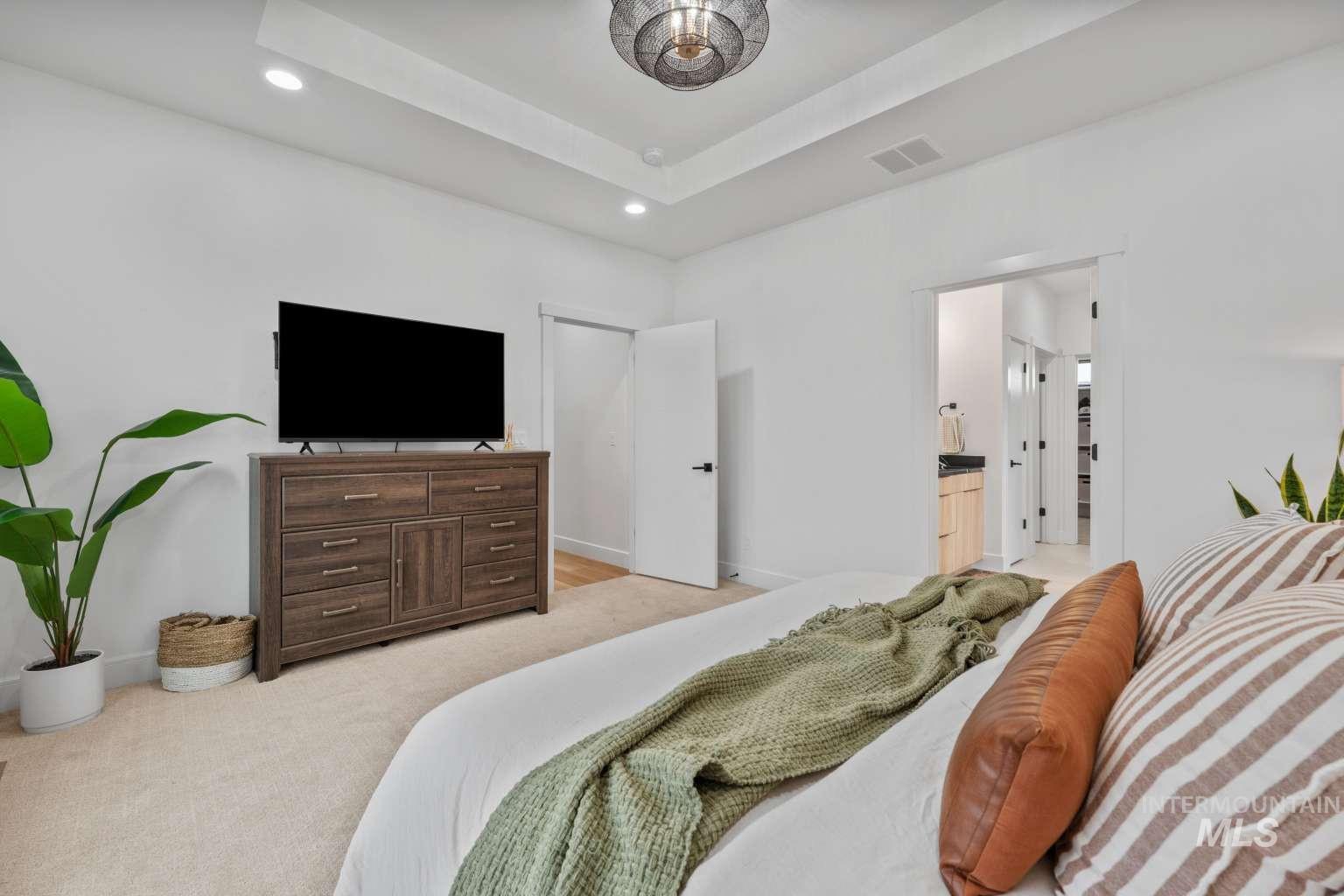 Bedroom featuring recessed lighting, light carpet, a raised ceiling, and ensuite bathroom