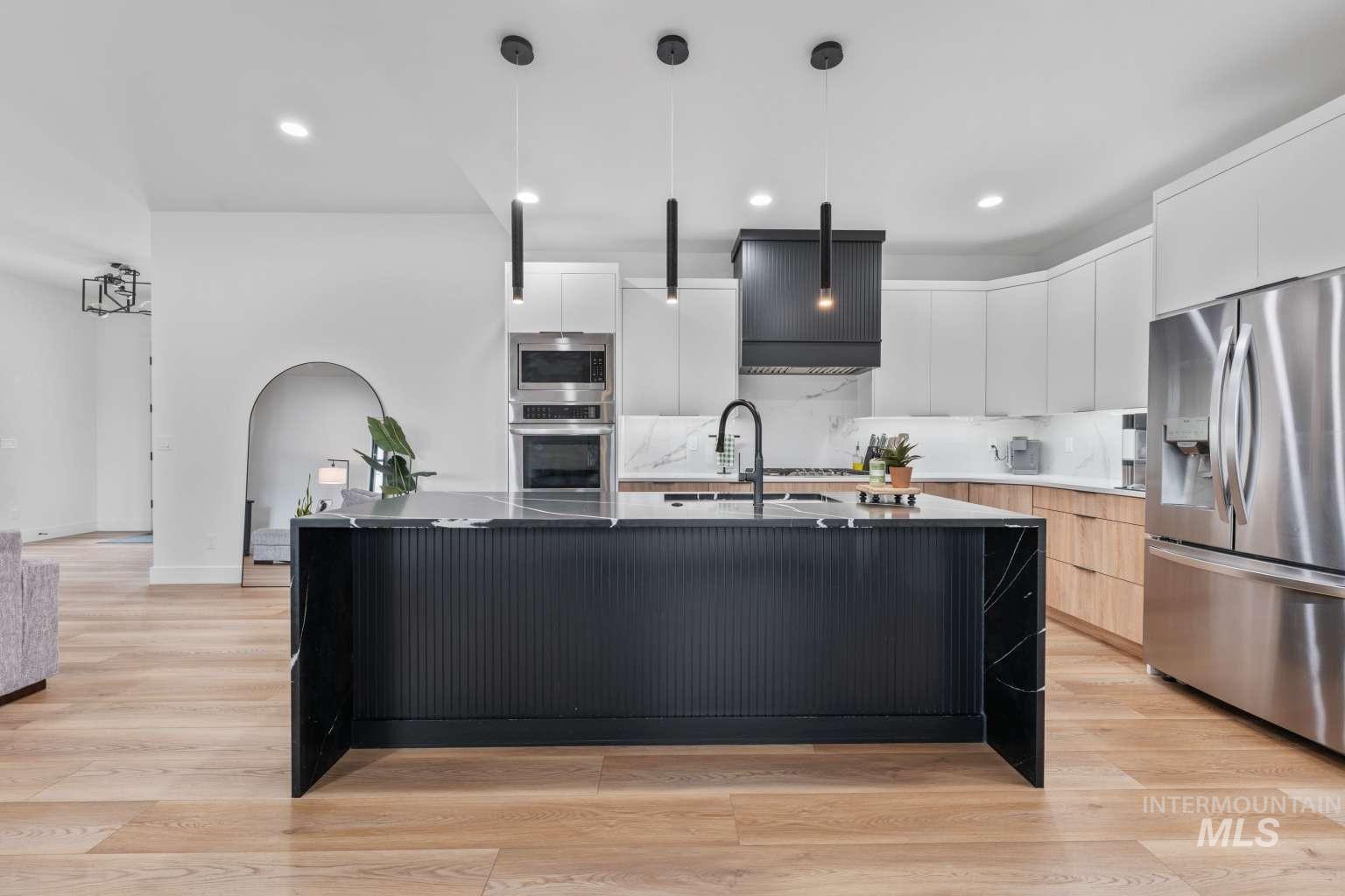 Kitchen with dual tone cabinetry, modern cabinets, stainless steel appliances, a large island with sink, and decorative light fixtures