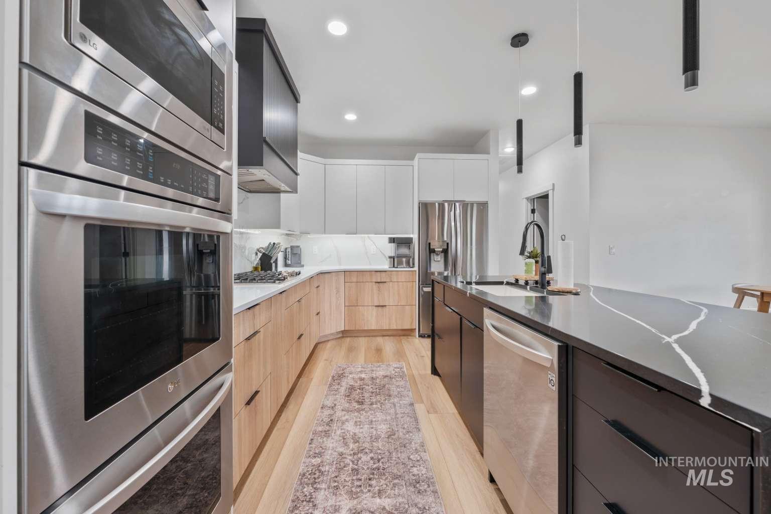 Kitchen with two tone cabinets, modern cabinets, stainless steel appliances, decorative light fixtures, and light wood-style floors