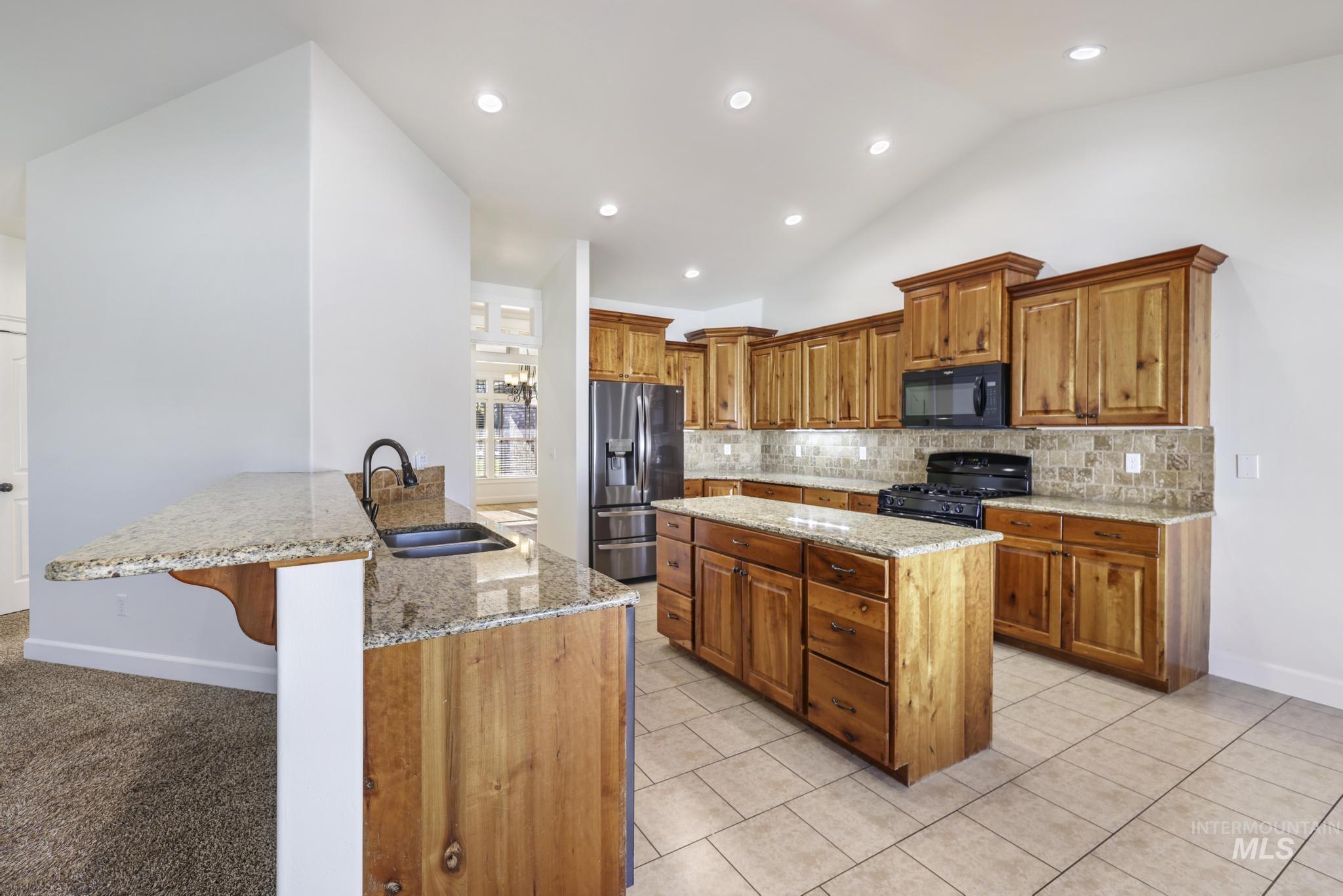 Kitchen featuring brown cabinets, light stone countertops, lofted ceiling, a kitchen breakfast bar, and tasteful backsplash