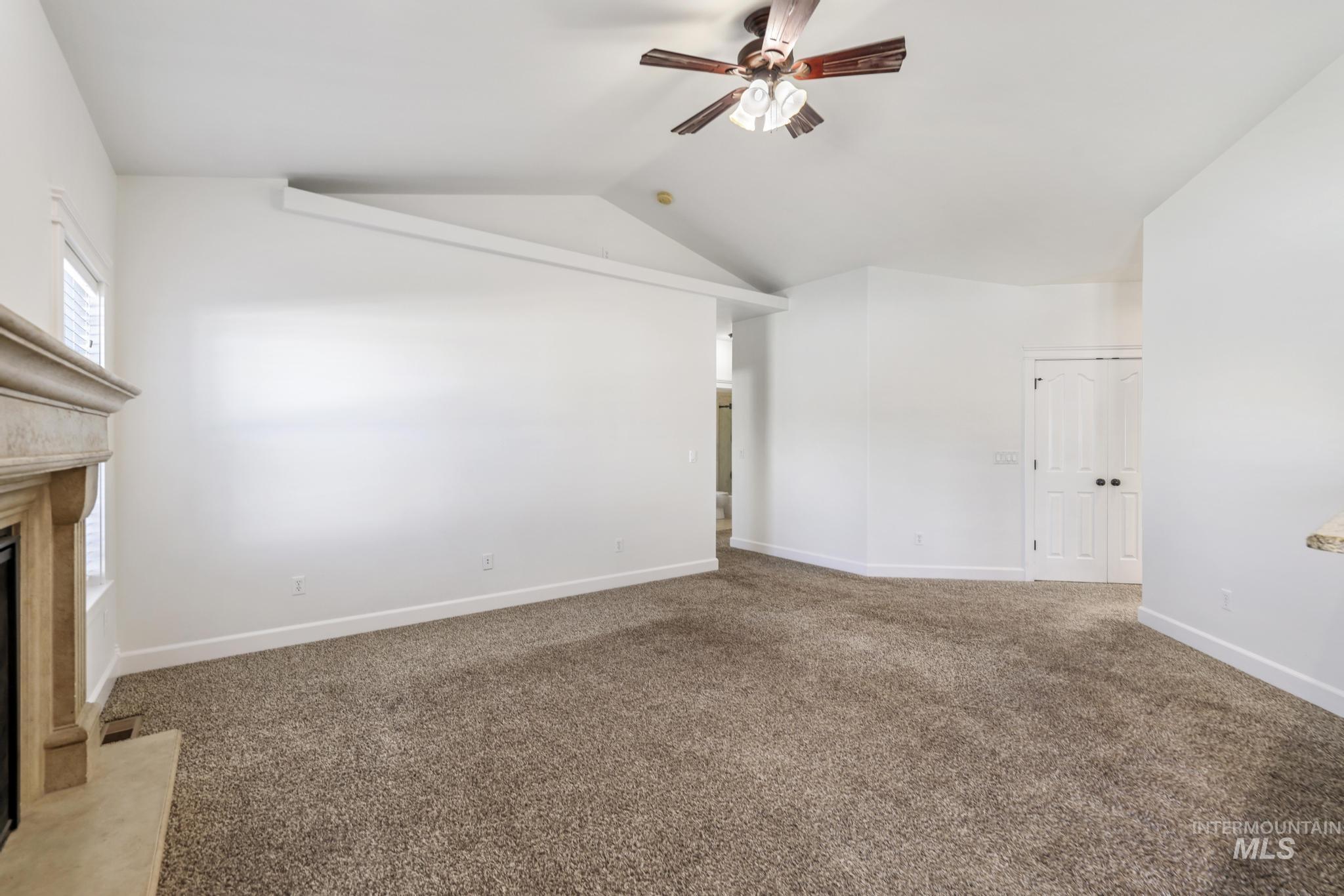 Unfurnished living room with light colored carpet, vaulted ceiling, a ceiling fan, and a premium fireplace