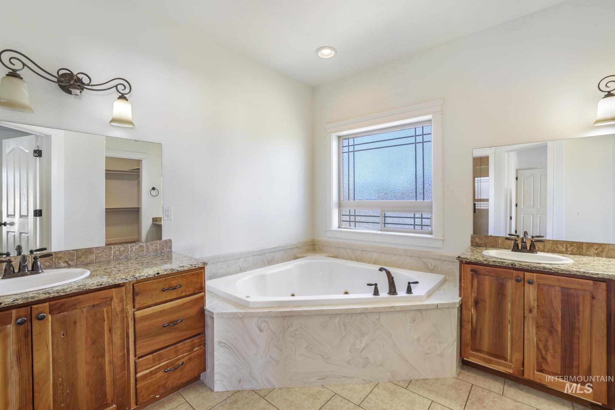 Full bath with two vanities, a jetted tub, light tile patterned floors, and a walk in closet