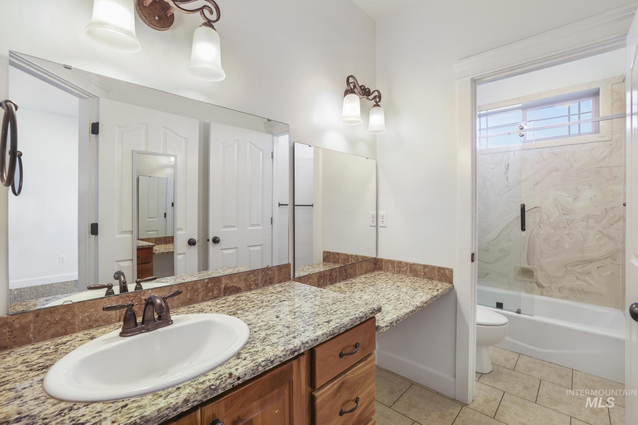 Full bath with bath / shower combo with glass door, vanity, and light tile patterned floors