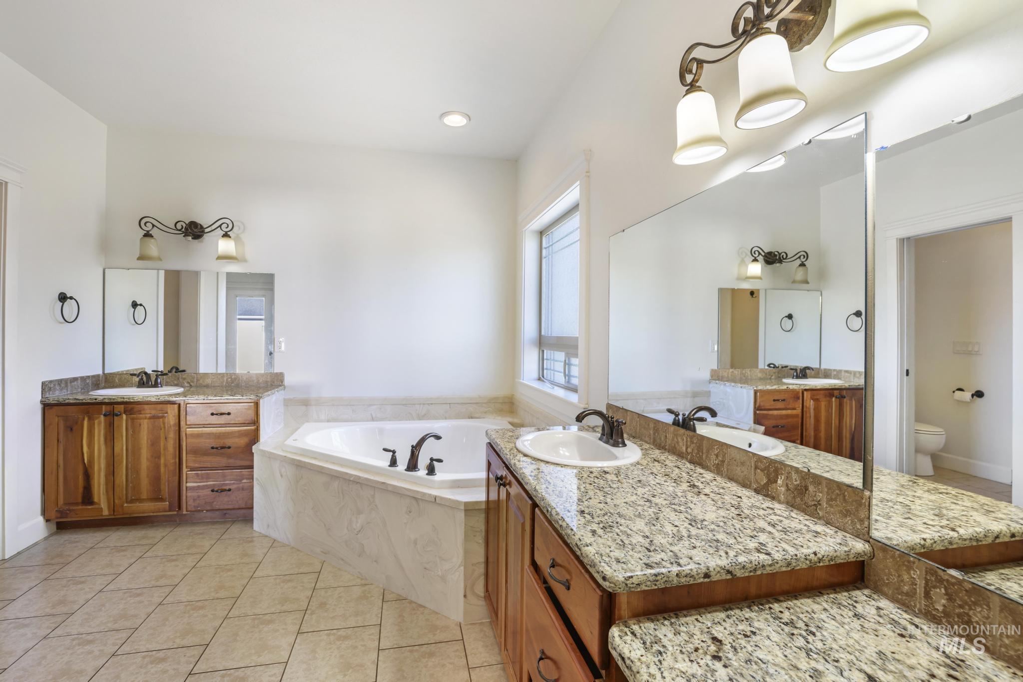Bathroom with two vanities, light tile patterned floors, a garden tub, and recessed lighting
