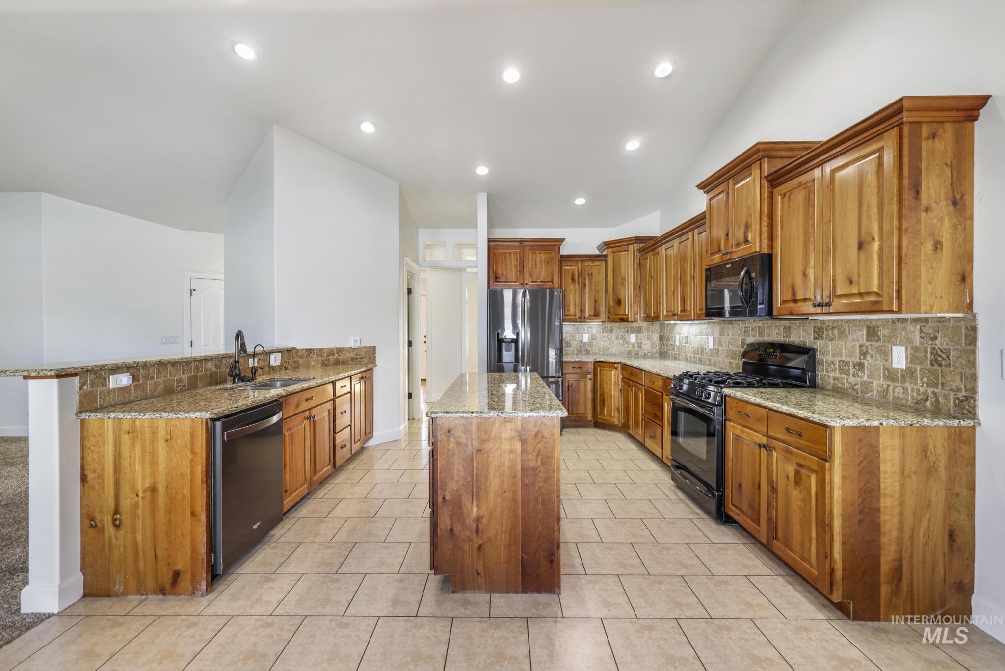 Kitchen featuring brown cabinets, light stone counters, black appliances, decorative backsplash, and recessed lighting
