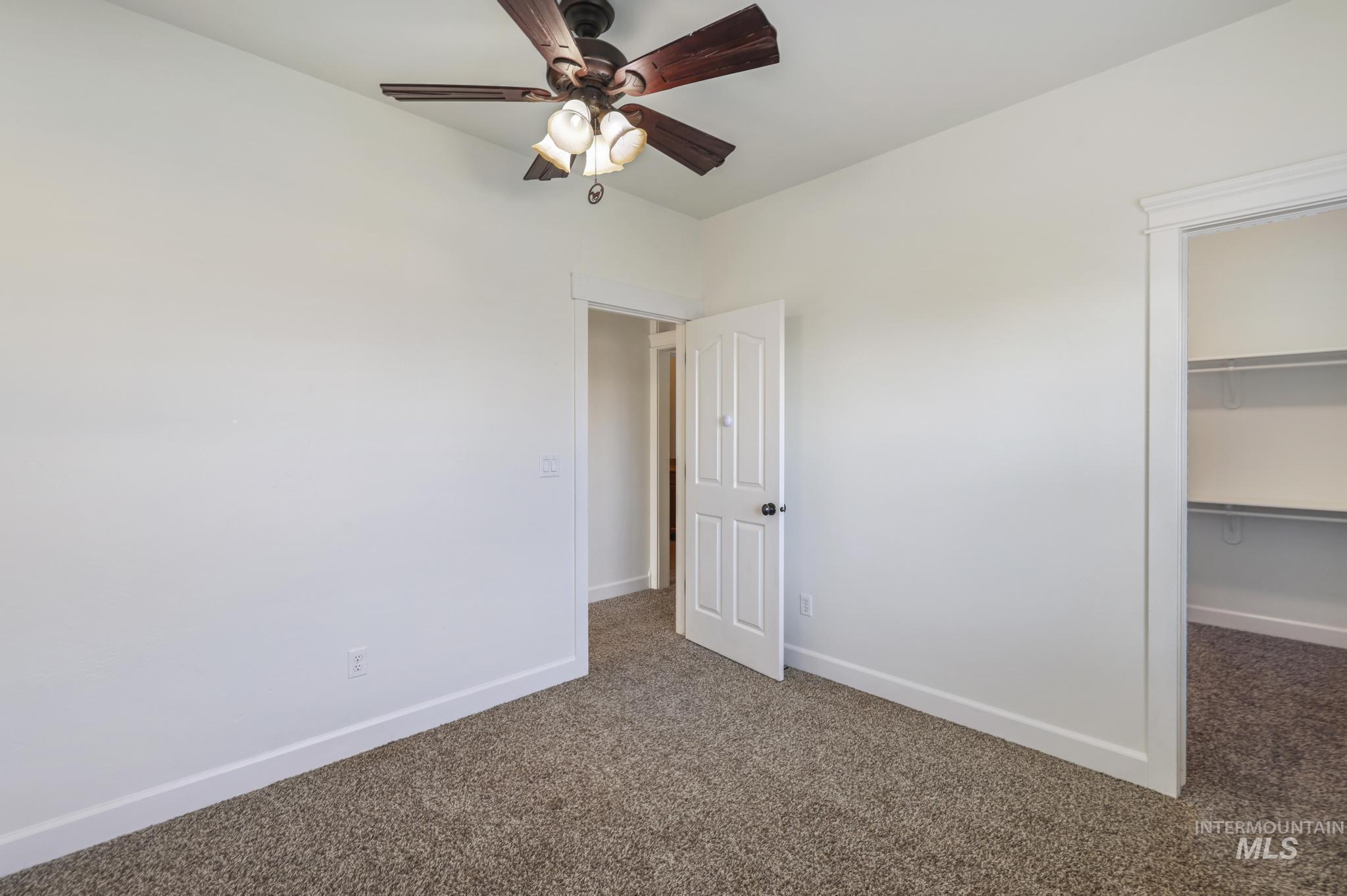 Unfurnished bedroom featuring dark carpet, a spacious closet, and ceiling fan