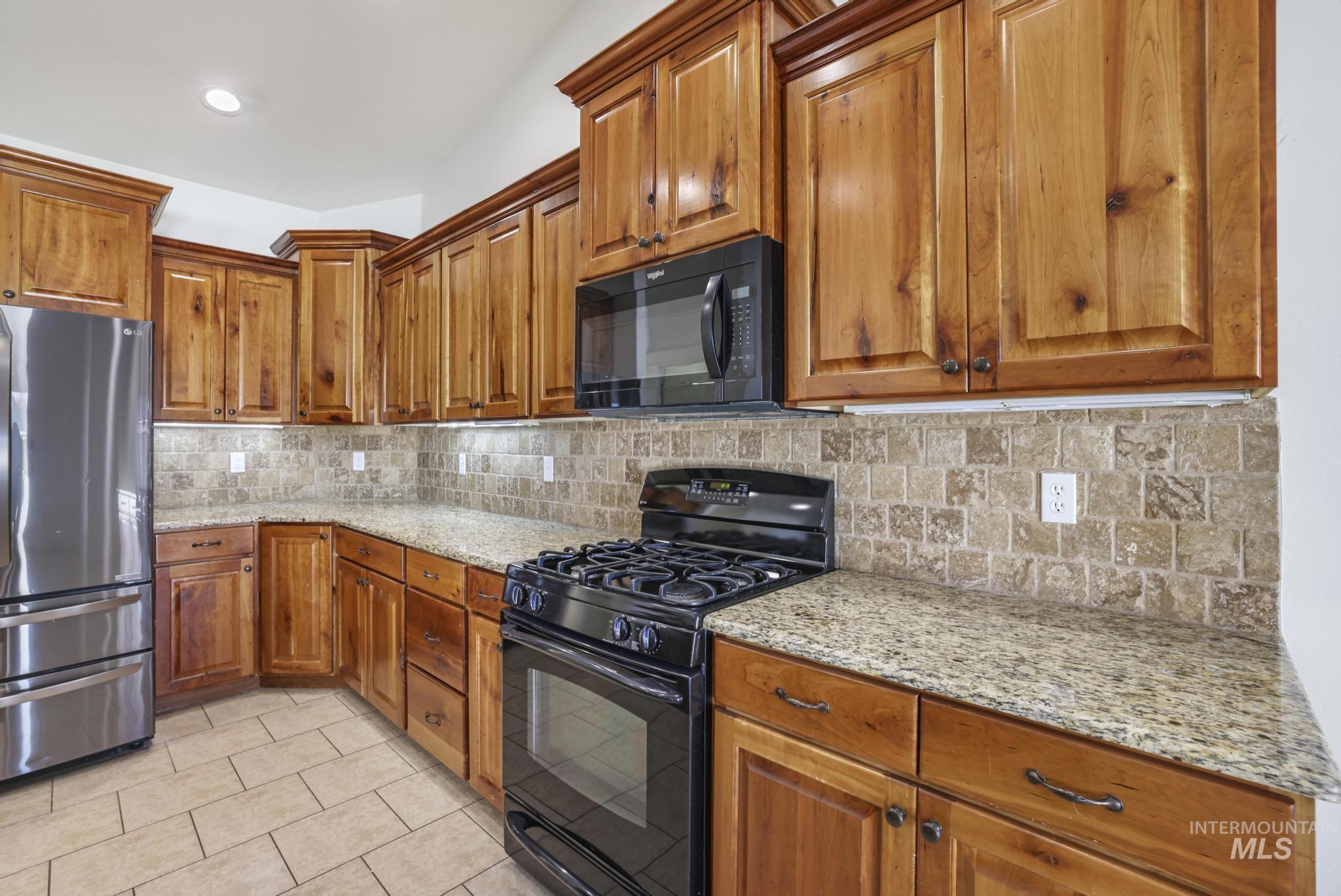 Kitchen with black appliances, brown cabinets, light stone counters, and tasteful backsplash