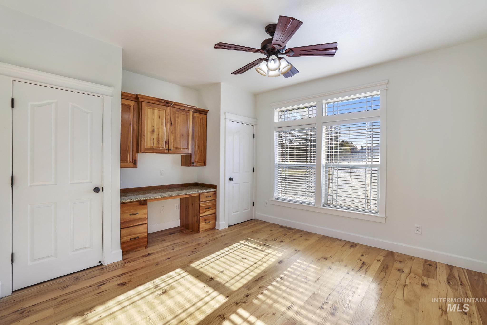 Unfurnished office featuring built in study area, light wood finished floors, and a ceiling fan
