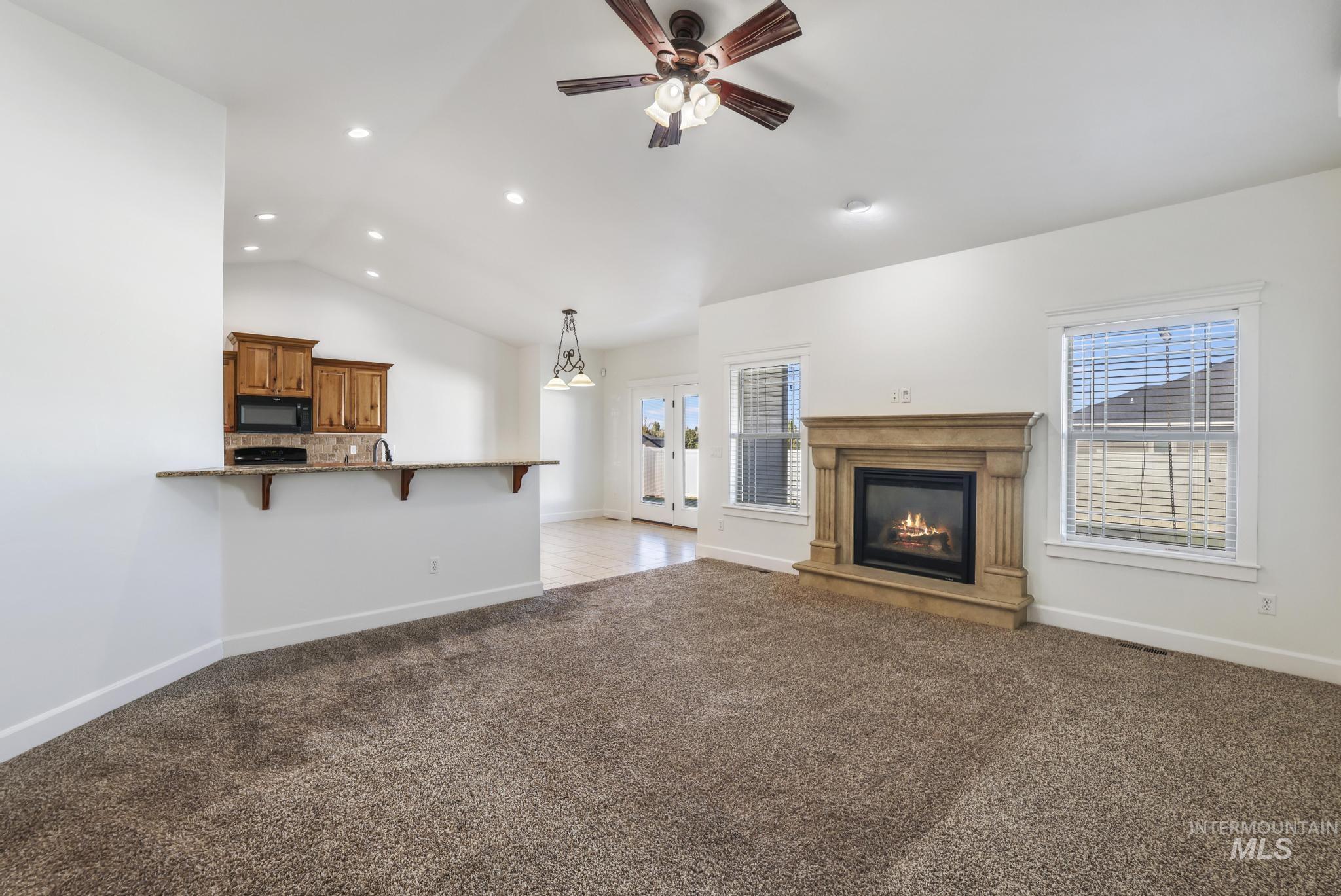 Unfurnished living room with dark colored carpet, a glass covered fireplace, vaulted ceiling, recessed lighting, and ceiling fan