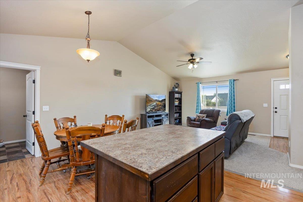 Kitchen with dark brown cabinets, a center island, decorative light fixtures, light wood-style flooring, and lofted ceiling