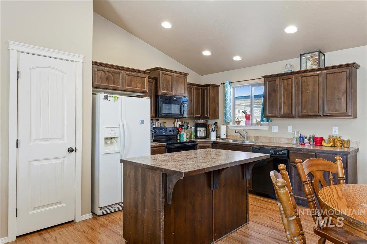 Kitchen featuring dark brown cabinets, a center island, black appliances, light wood finished floors, and vaulted ceiling