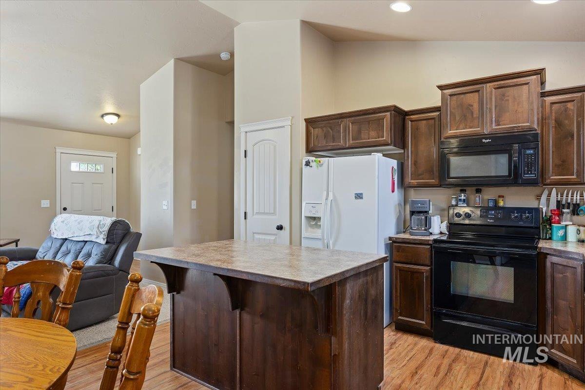 Kitchen with dark brown cabinets, black appliances, vaulted ceiling, a kitchen island, and a kitchen bar