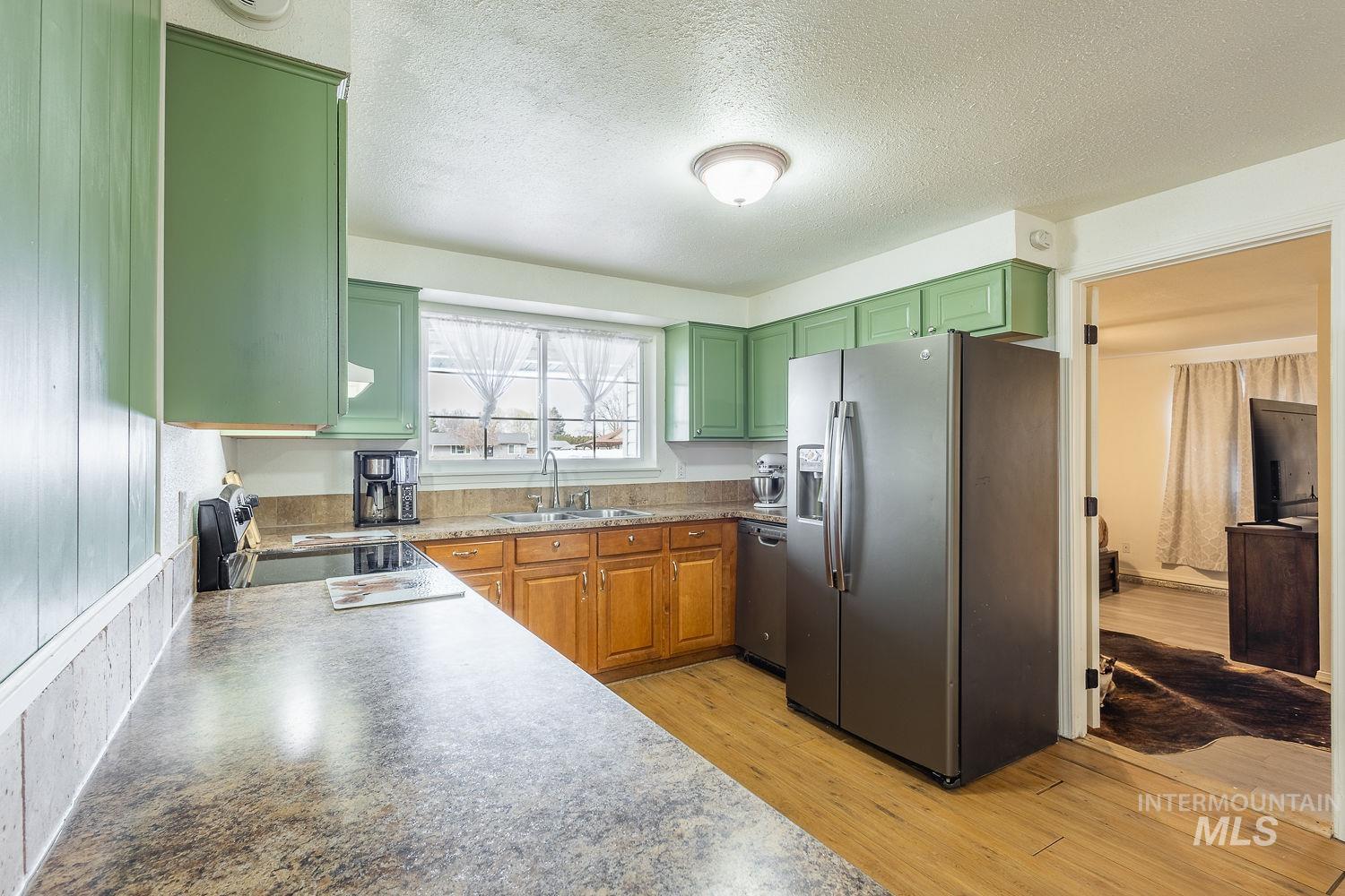 Kitchen with stainless steel appliances, light wood-type flooring, a textured ceiling, green cabinets, and wood finish cabinets