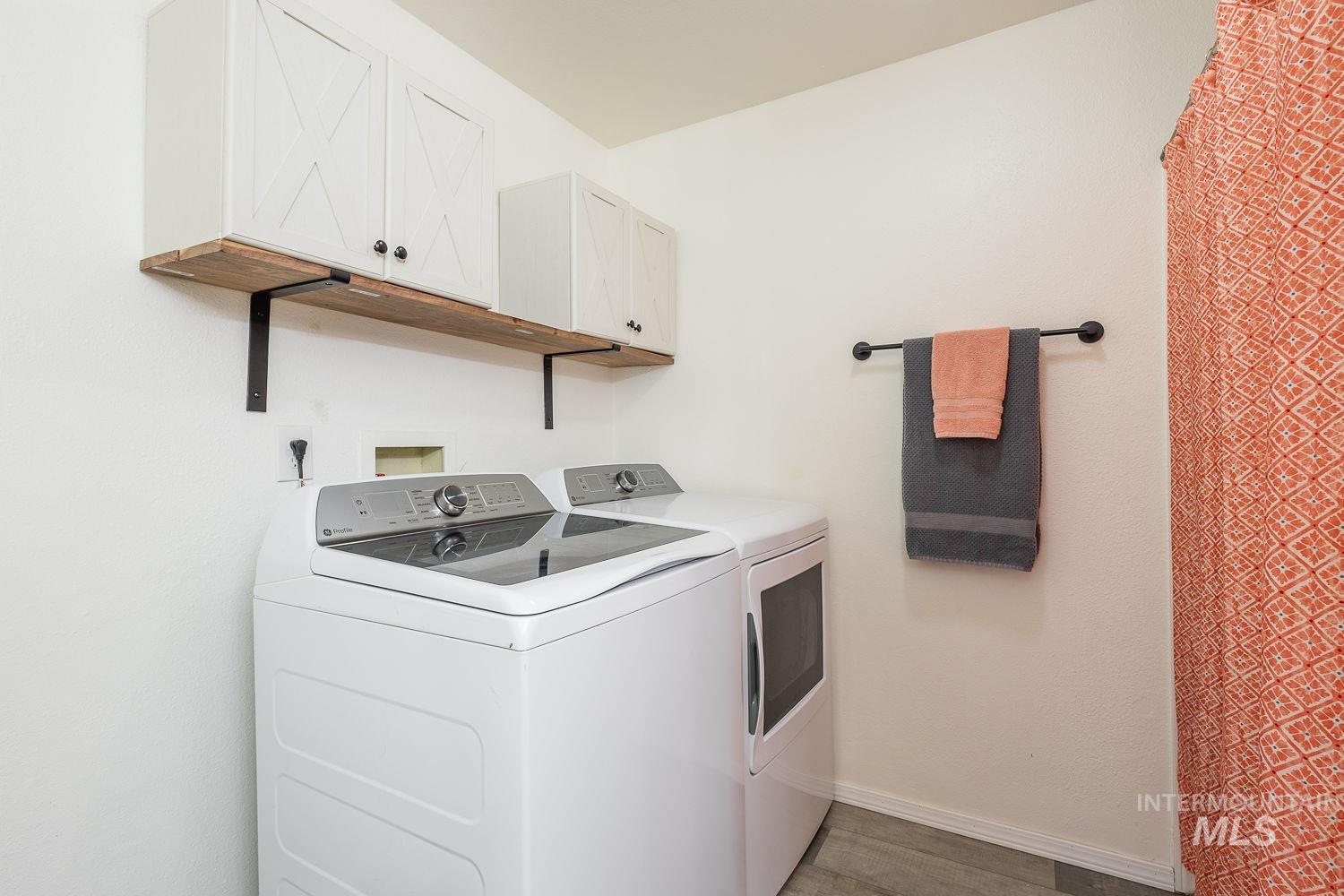 Laundry area with separate washer and dryer, cabinet space, and light wood finished floors