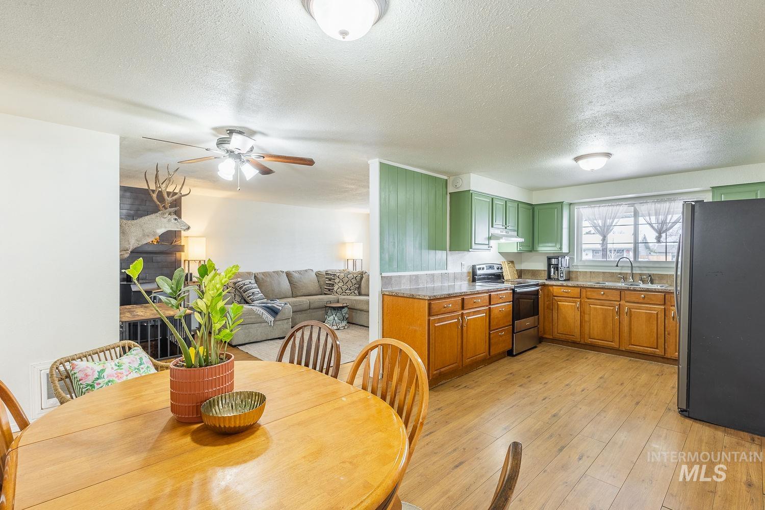 Kitchen featuring stainless steel appliances, light wood-style floors, a textured ceiling, a fireplace, and a ceiling fan
